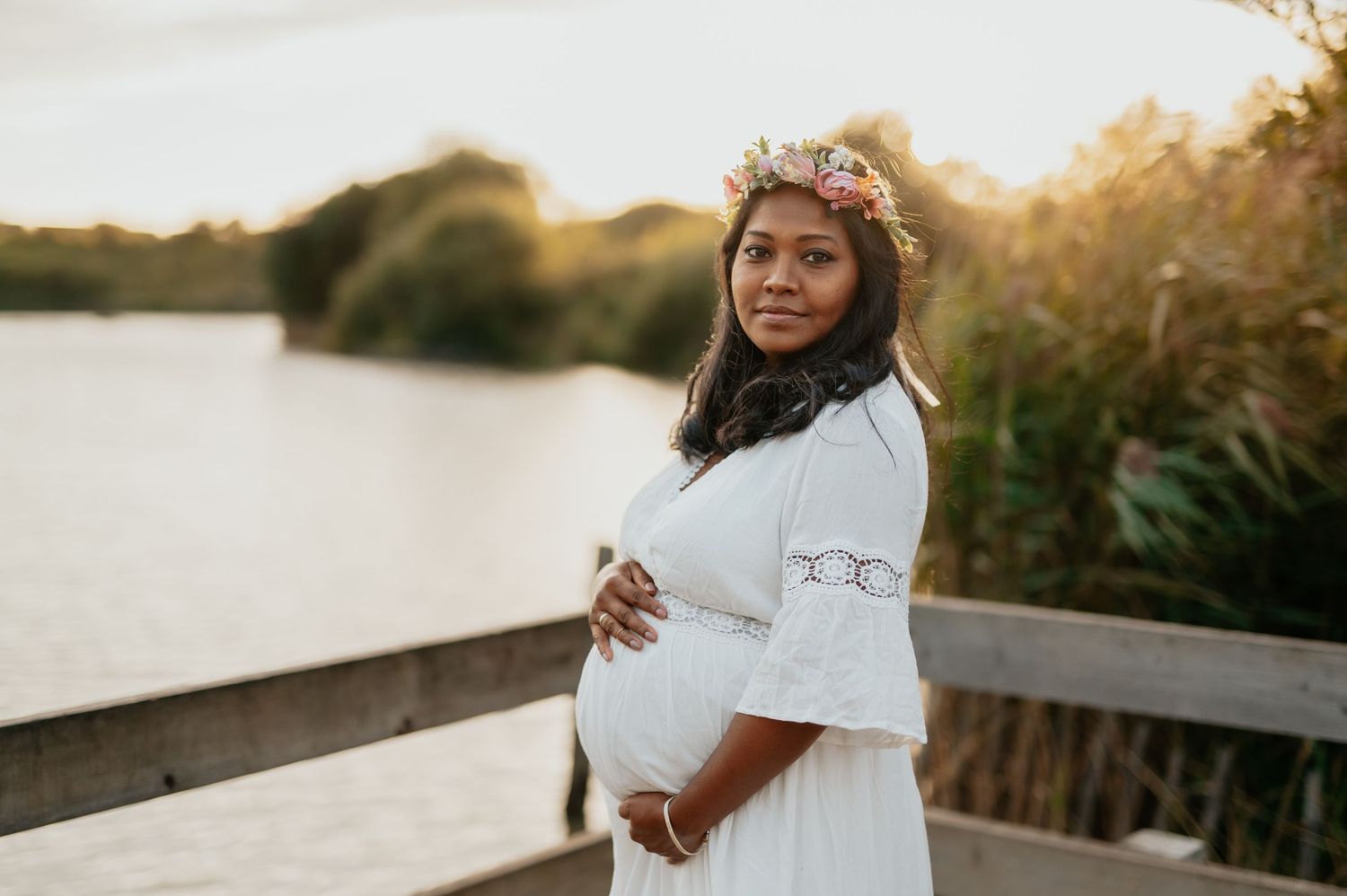 Ethereal maternity session in white dress among wildflowers at sunset.