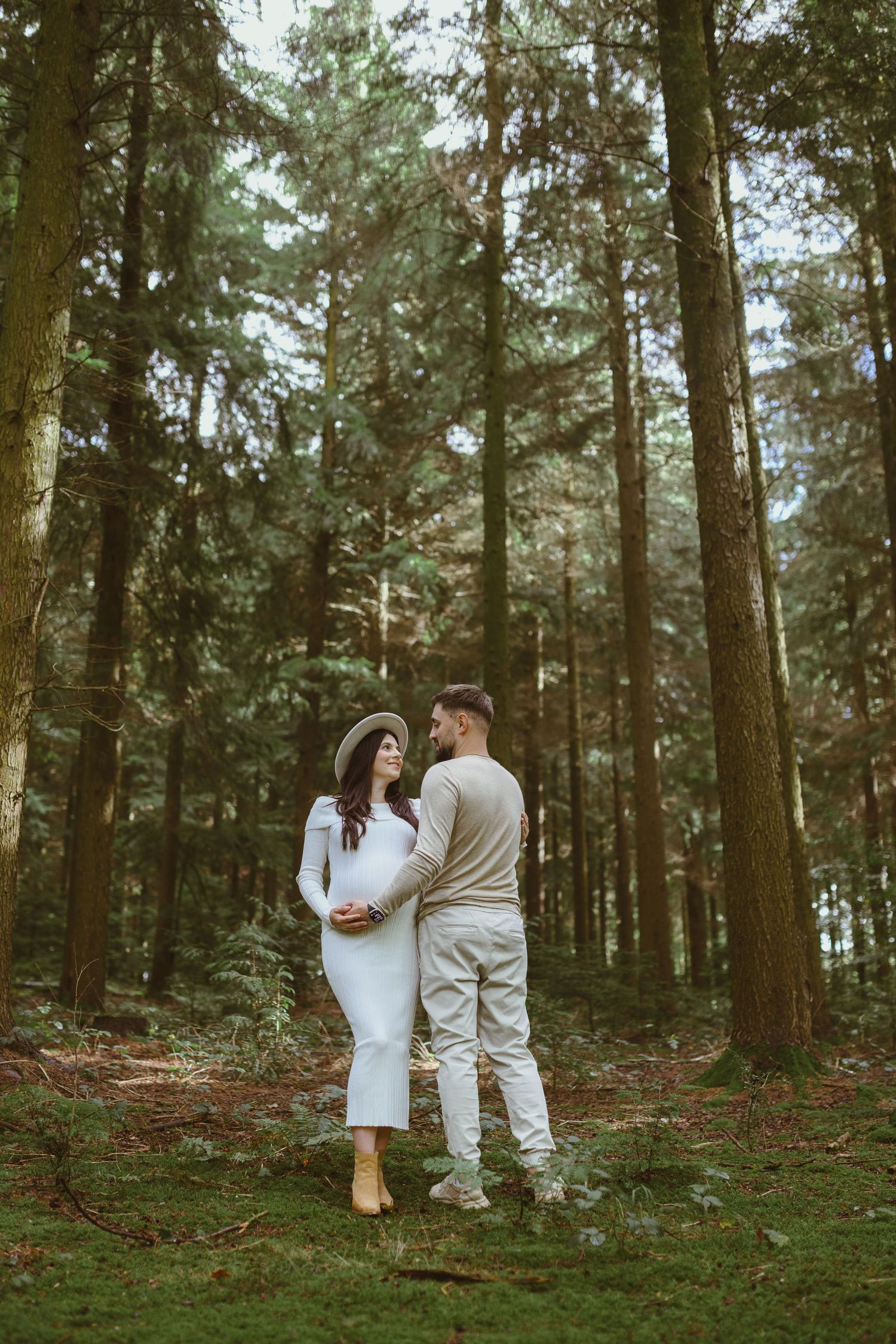 Couple walking through misty evergreen forest in matching white outfits.