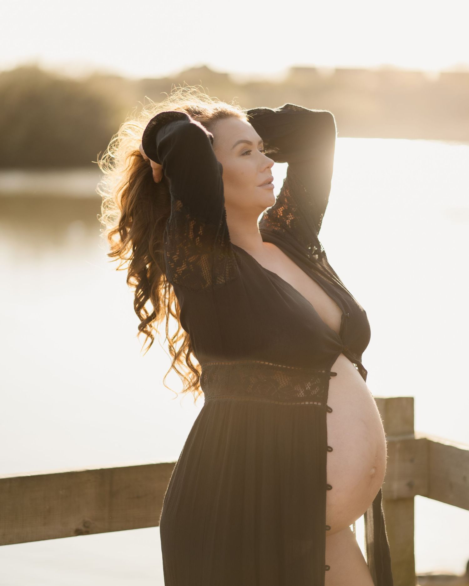 Silhouetted maternity portraits at sunset against water and wooden railing.