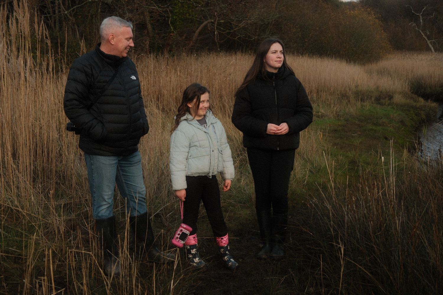 People gathered outdoors at dusk near tall grass and natural scenery.
