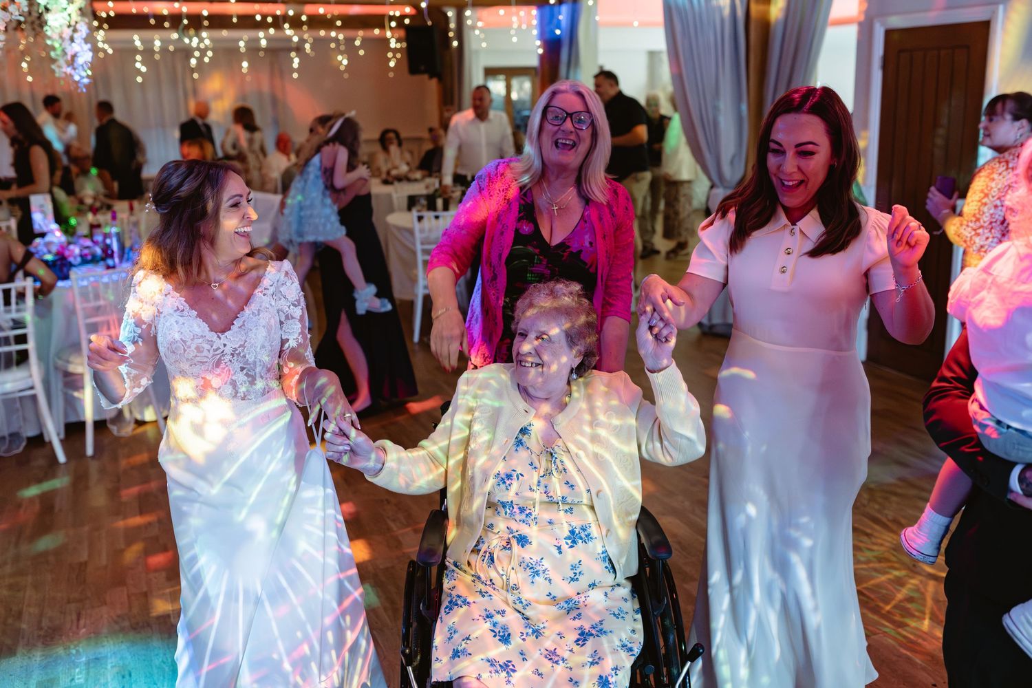 Wedding guests dancing and celebrating on the dance floor under colorful party lights.