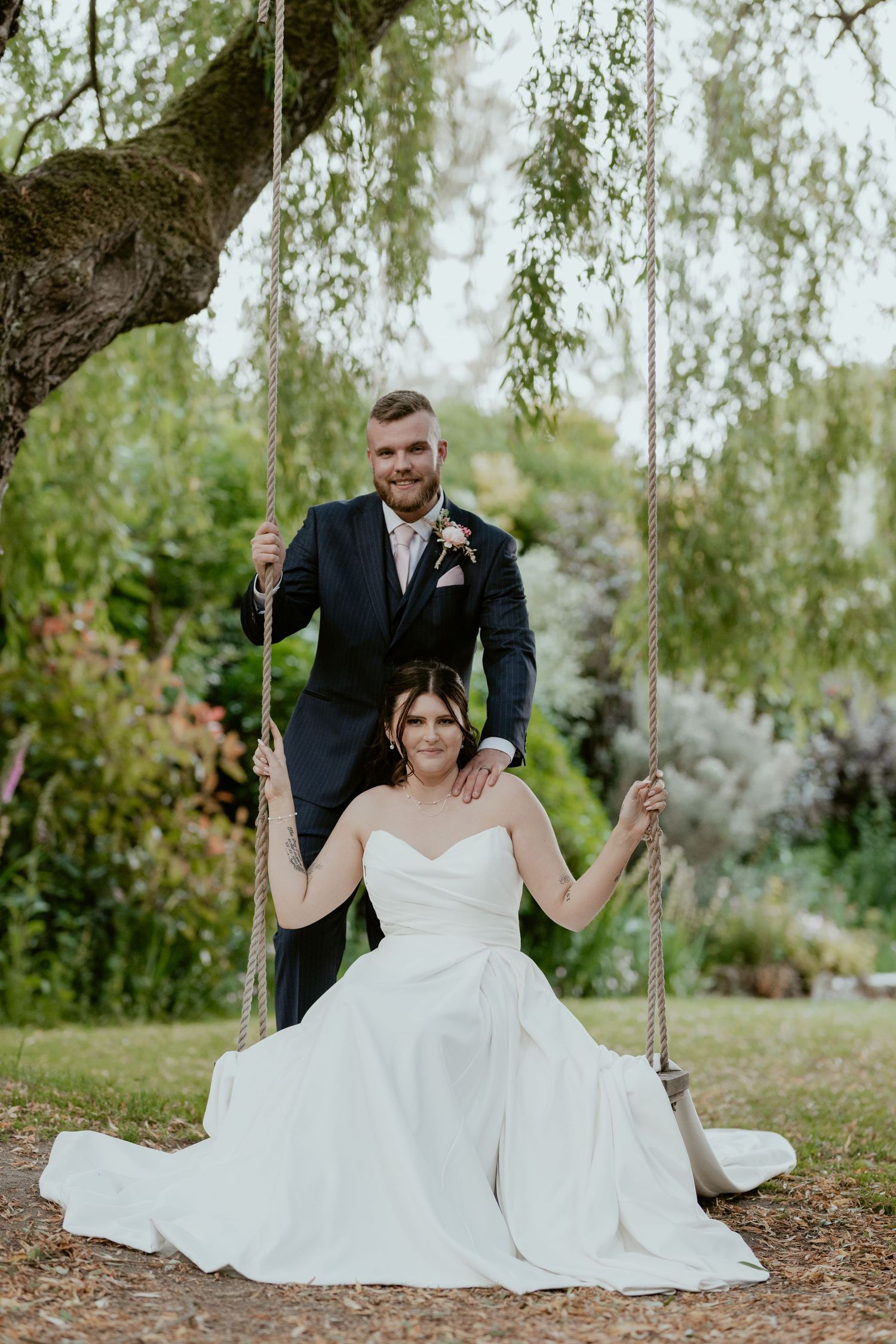 Couple enjoying playful moments on a tree swing in a garden setting.