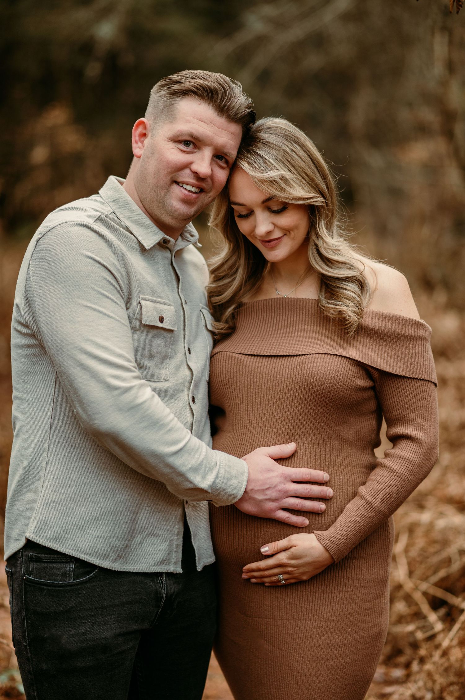 A tender maternity moment captured between a couple in warm earth tones against a natural backdrop.