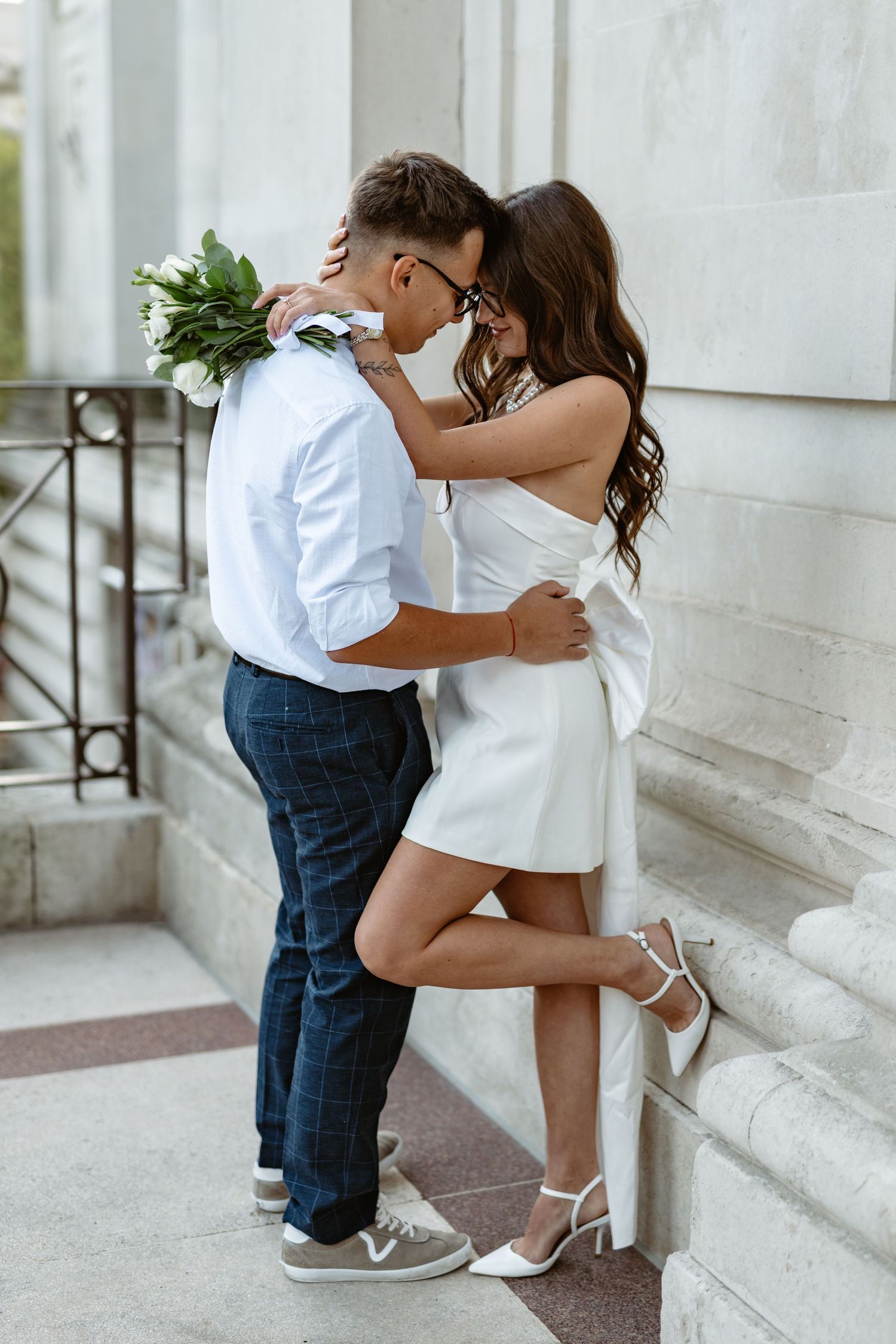 Romantic couple in white and blue outfits embrace on elegant stone steps during an engagement photoshoot.
