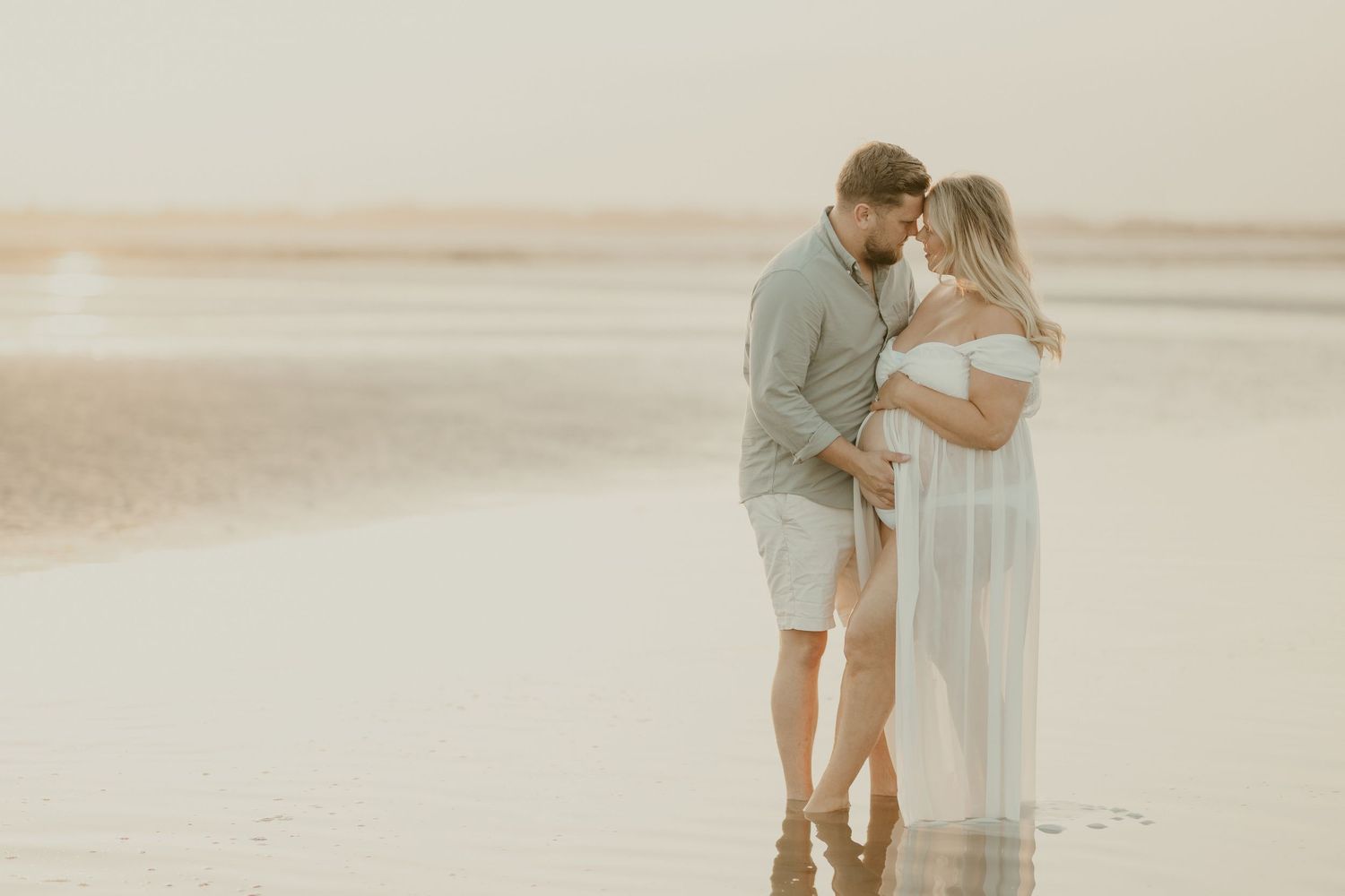 Intimate couple's portrait at sunset on beach in soft muted tones.