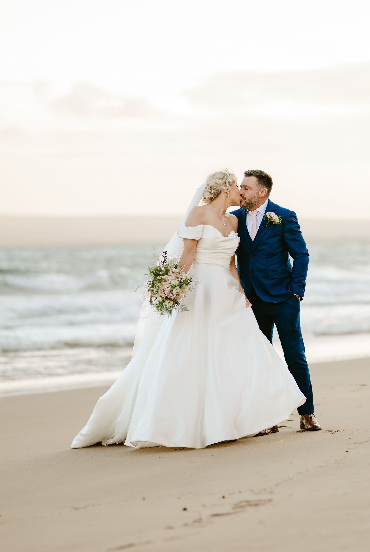 Romantic beach wedding portraits with couple in white gown and navy suit.