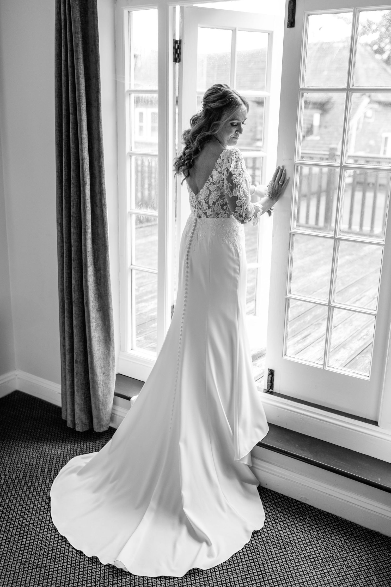 Elegant wedding dress with lace details and flowing train silhouetted against French doors.