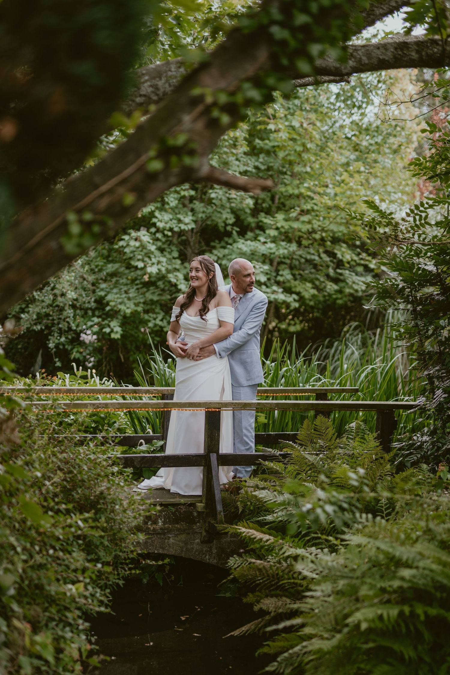 Wedding couple shares an intimate moment on a wooden bridge in a verdant garden setting.