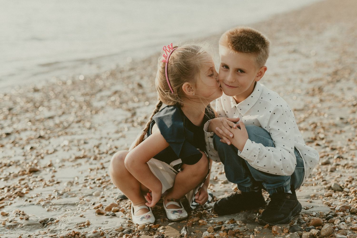 Two children share a sweet moment while playing on a sunlit beach.