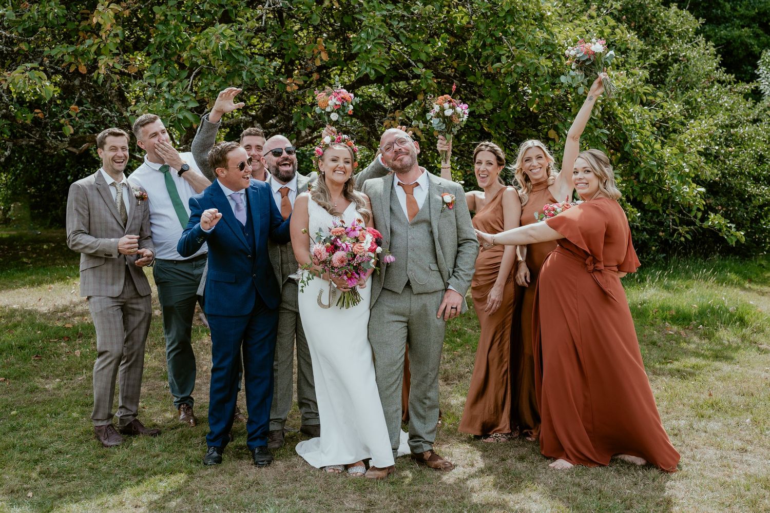 Wedding party poses in a garden setting wearing rust and grey attire.