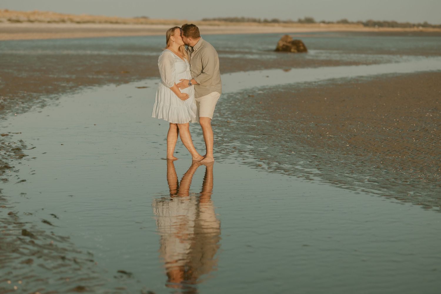 Beach photoshoot at golden hour with reflections in shallow water.