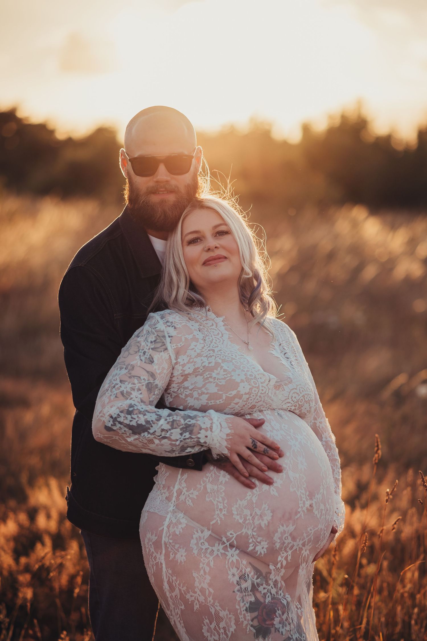 Intimate maternity portrait in a sunlit field during golden hour.