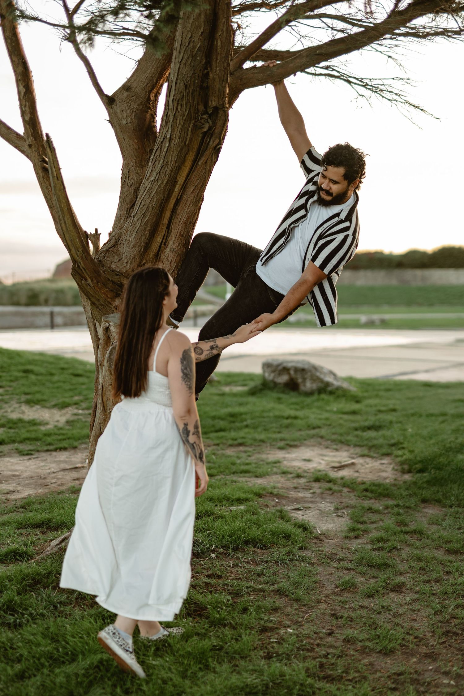 A couple poses playfully near a weathered tree during a coastal photoshoot.