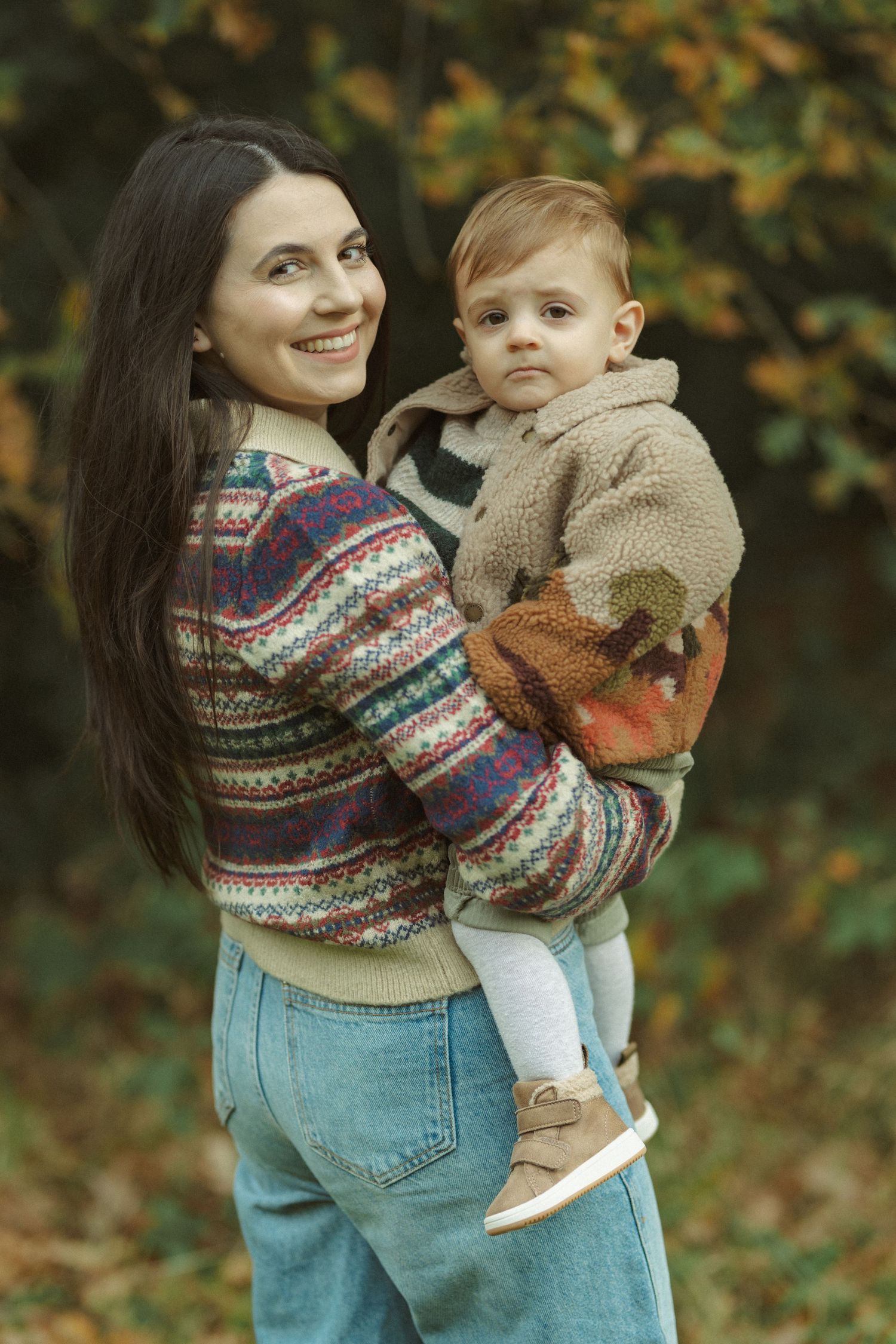 Family moments captured in fall setting with matching knit sweaters and autumn foliage.