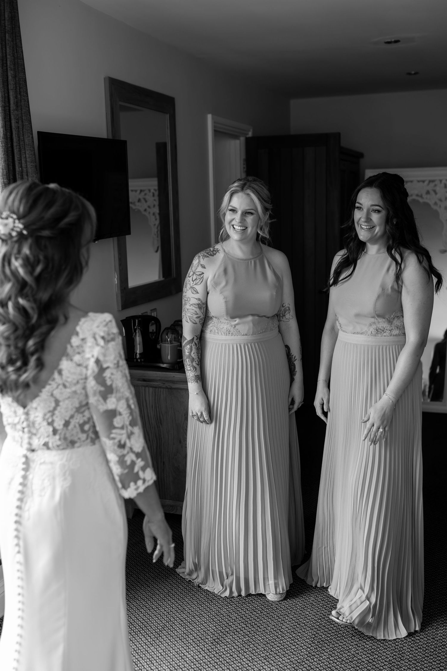 Elegant bridesmaids in pleated mauve dresses gather in a hotel room before the ceremony.