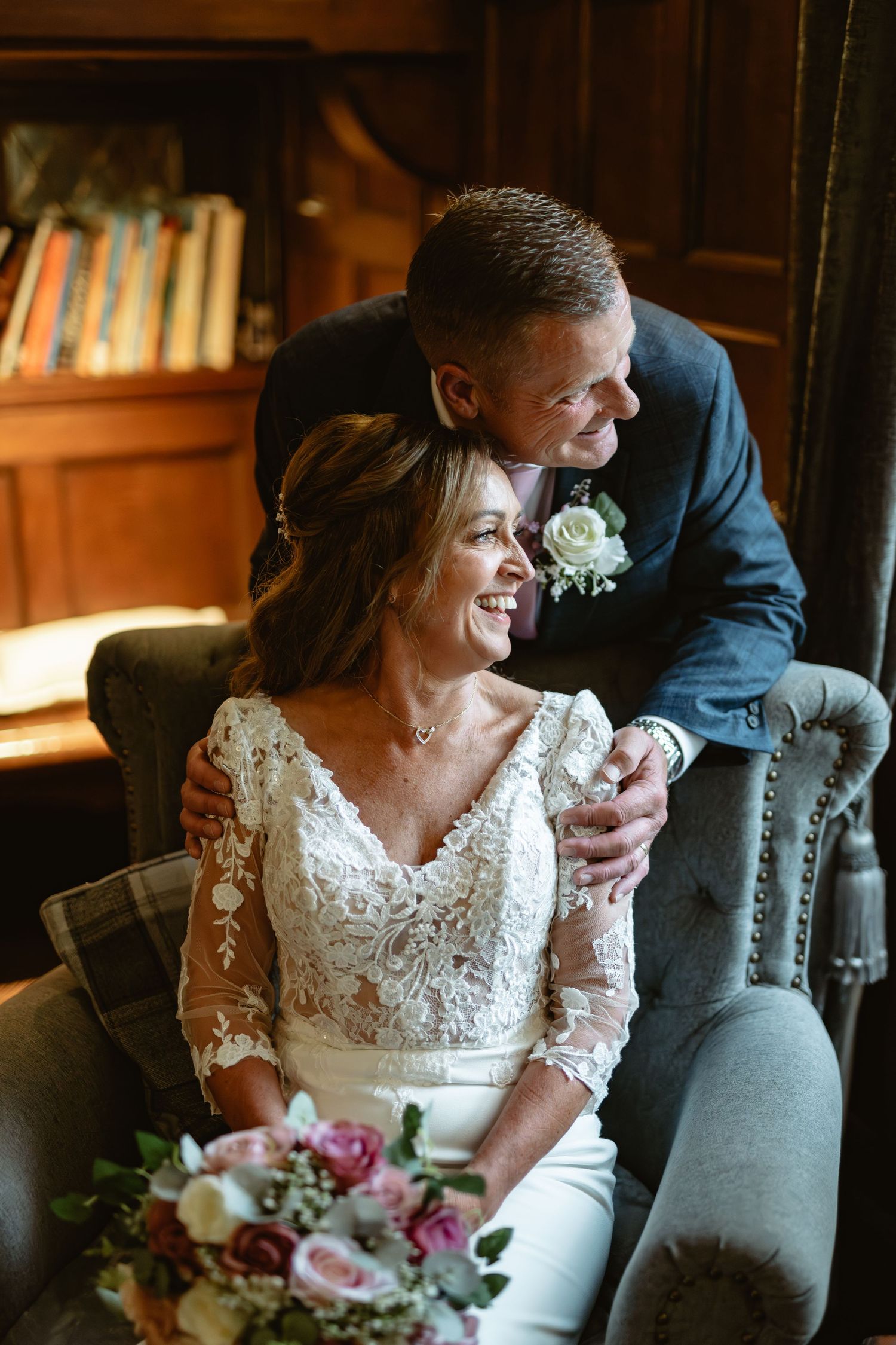 Newlyweds share intimate moments on grey couch in library setting.