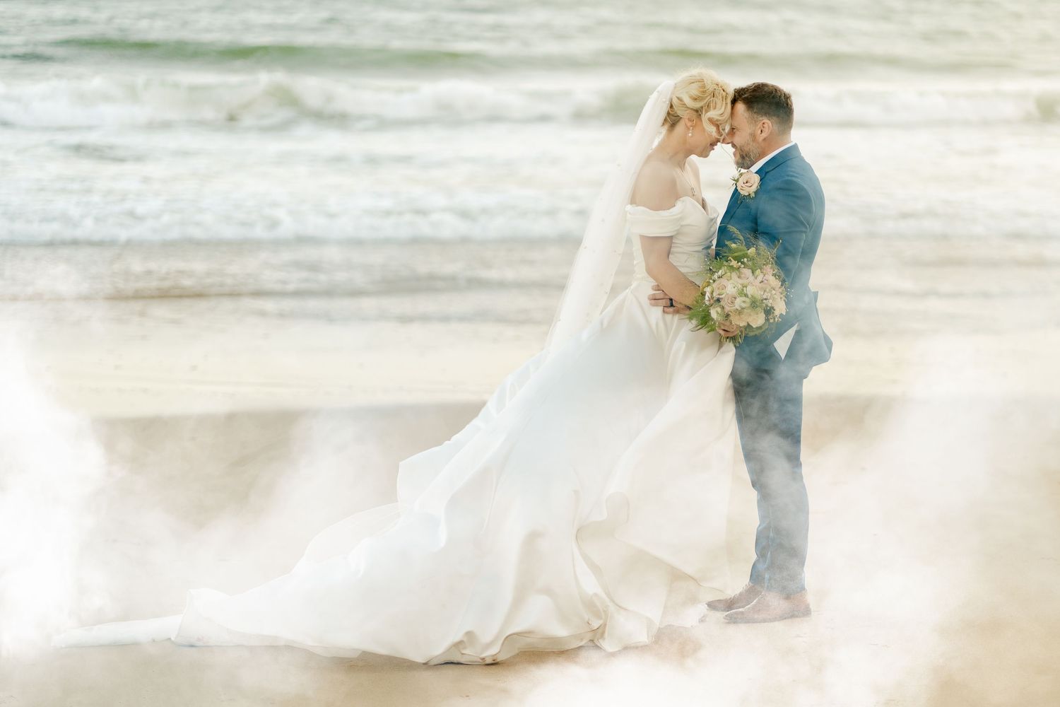 Romantic beach wedding photoshoot with flowing white dress and crashing waves in the background.