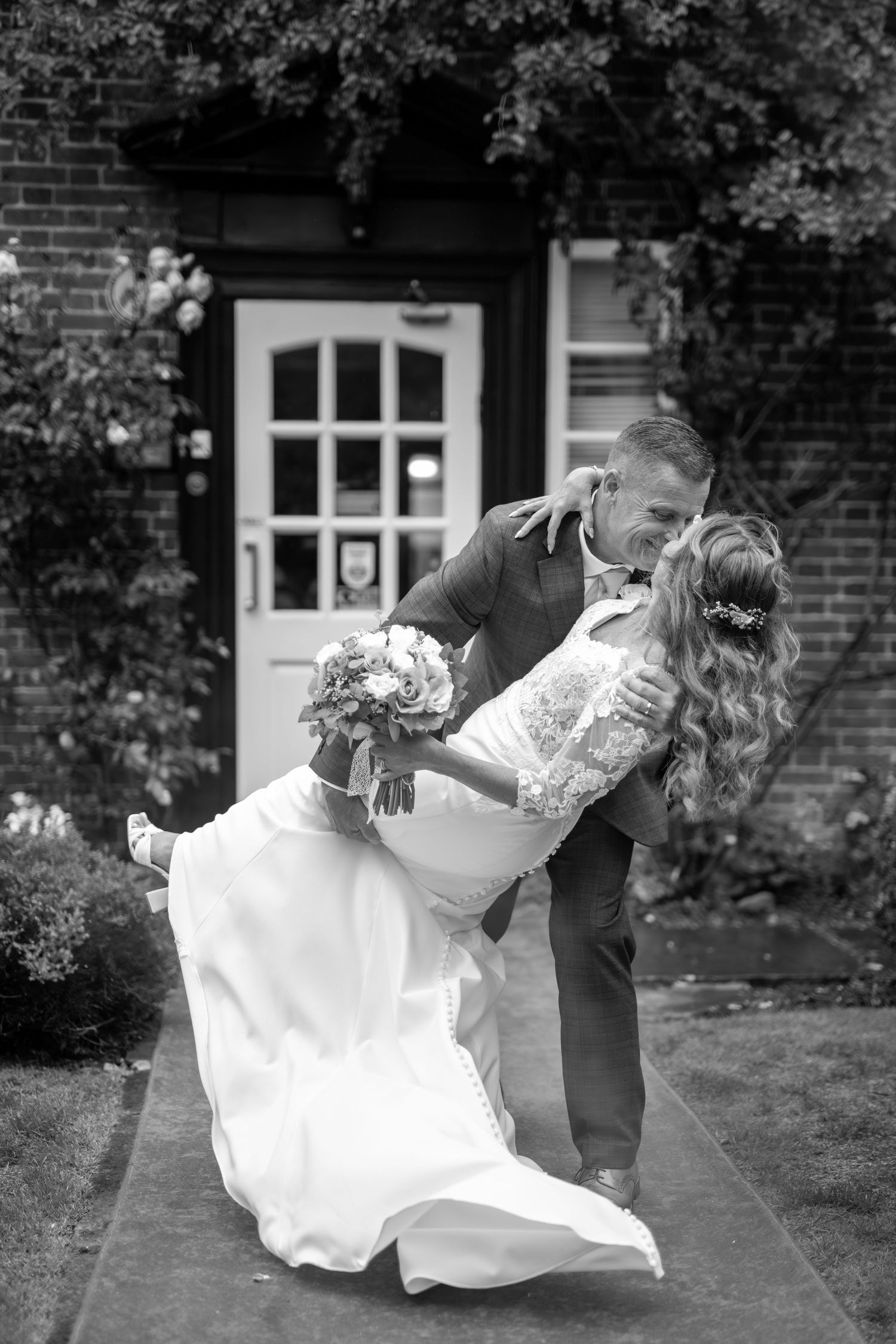 A couple performs a dramatic dance dip on a red carpet in front of a brick building with white trim.