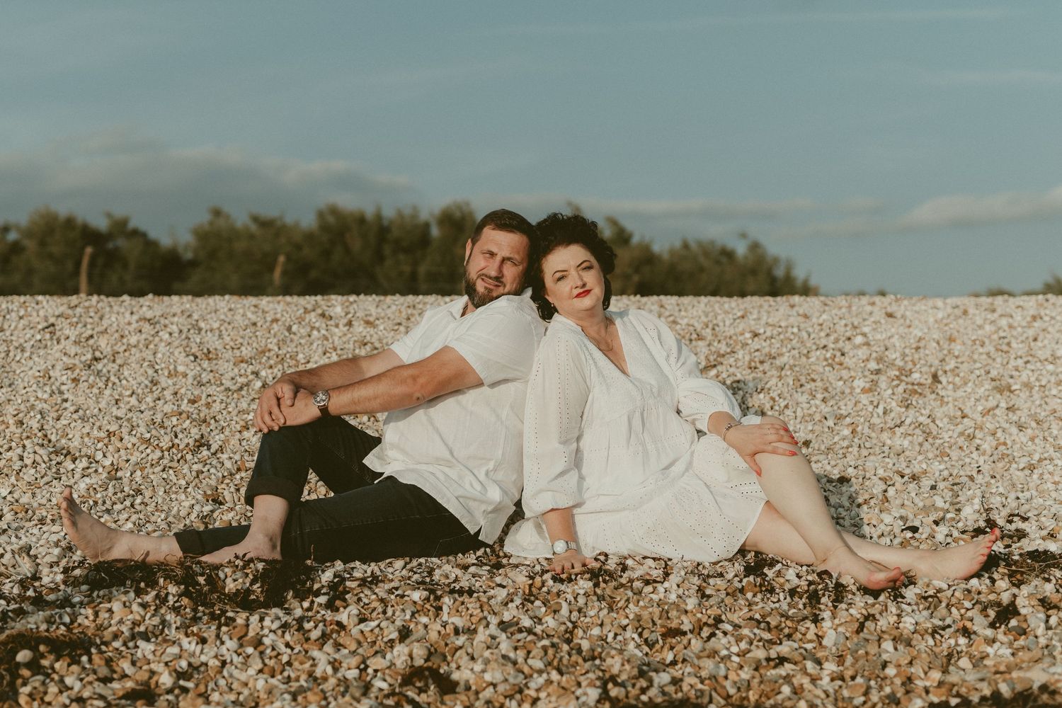 A relaxed couple lounging on a pebbly beach during sunset.