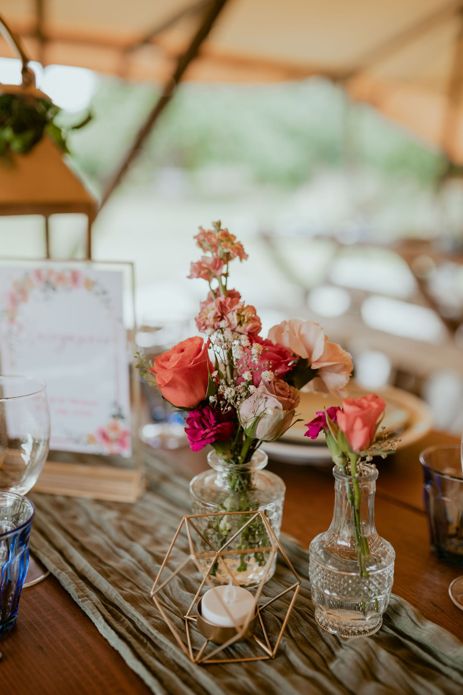 Wedding table centerpiece with coral roses in vintage glass vases and geometric accents.