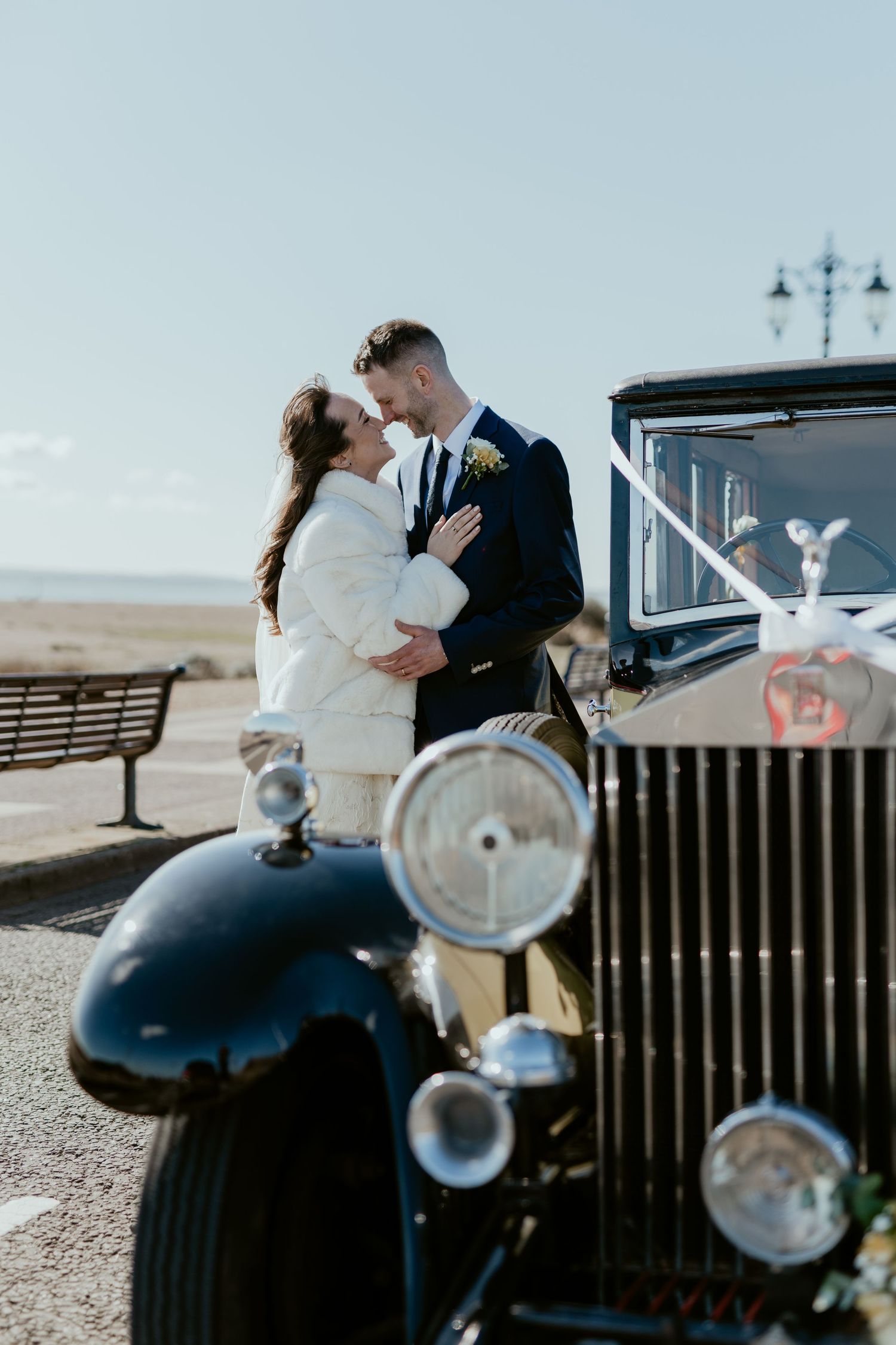 Romantic seaside wedding portraits with classic car and coastal backdrop.