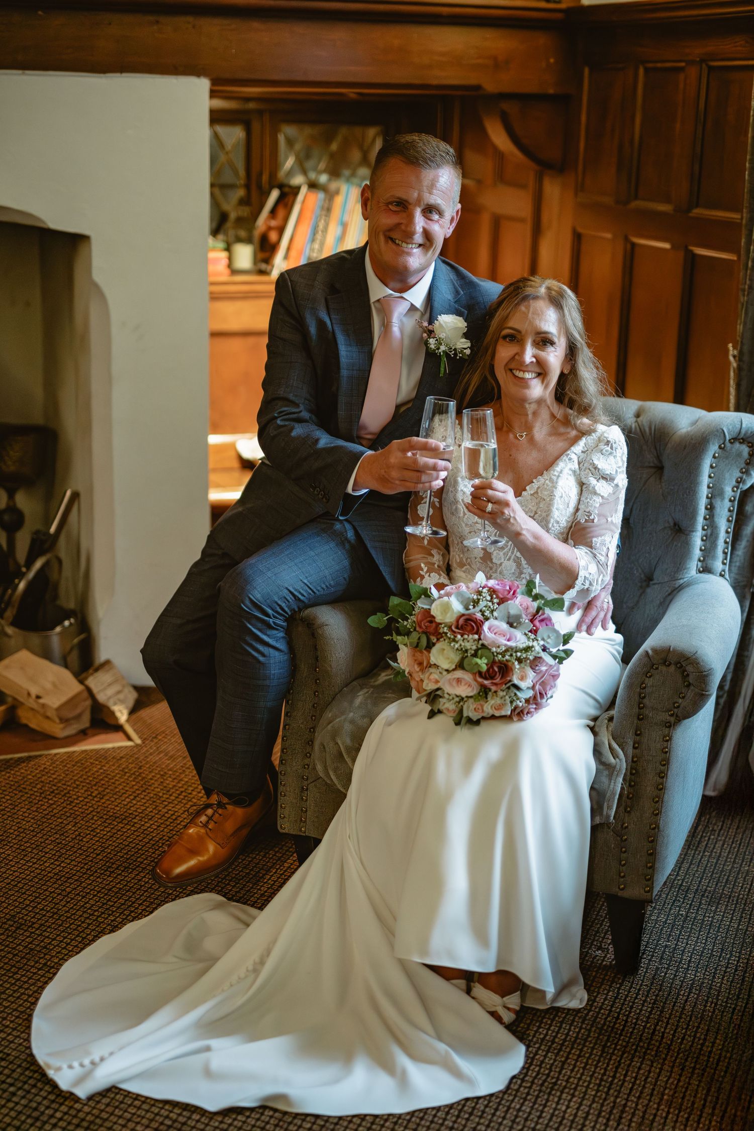 Wedding couple relaxing on grey armchair in elegant library setting.