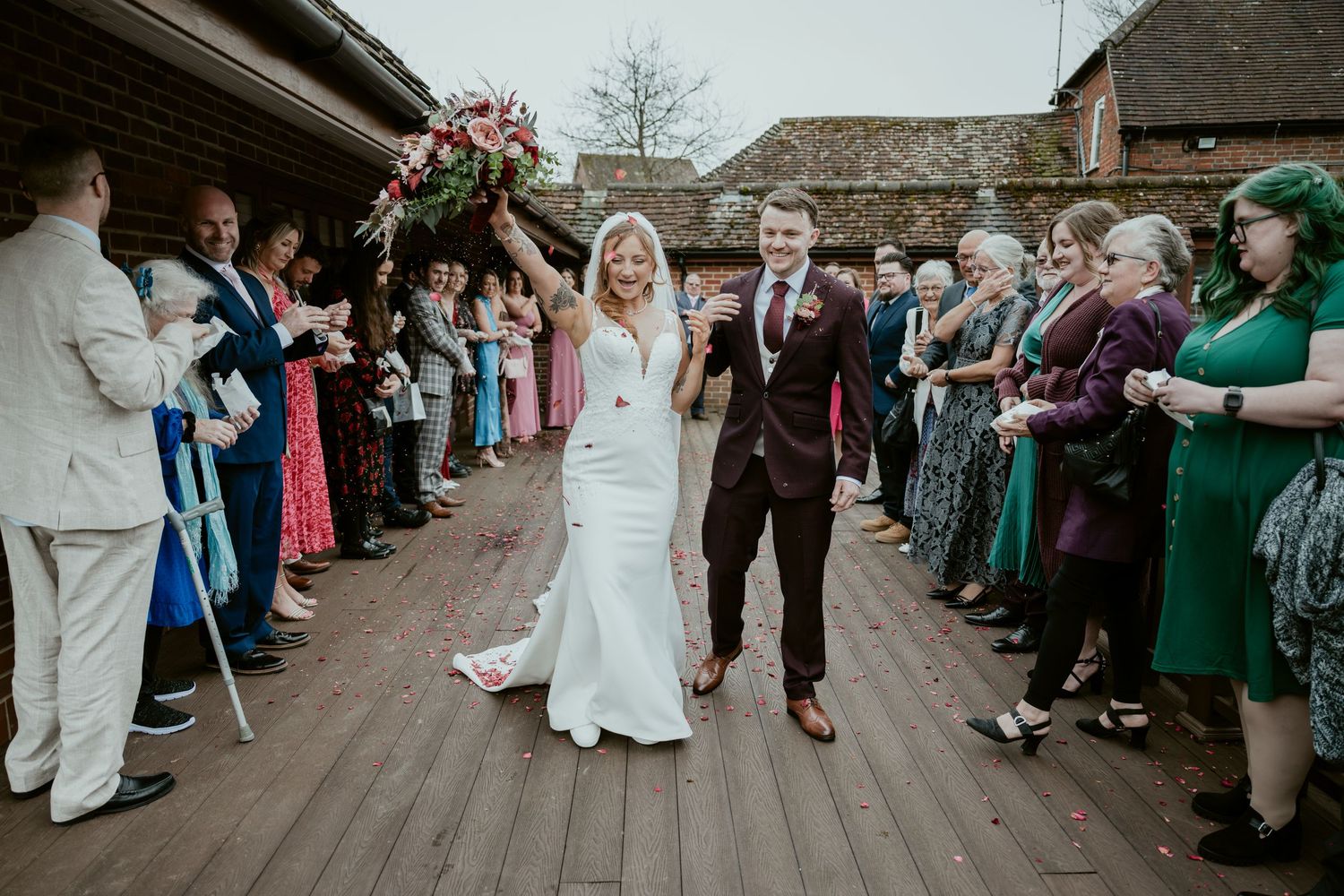 Wedding guests line up along a rustic stone path to celebrate the newlyweds during an outdoor ceremony.