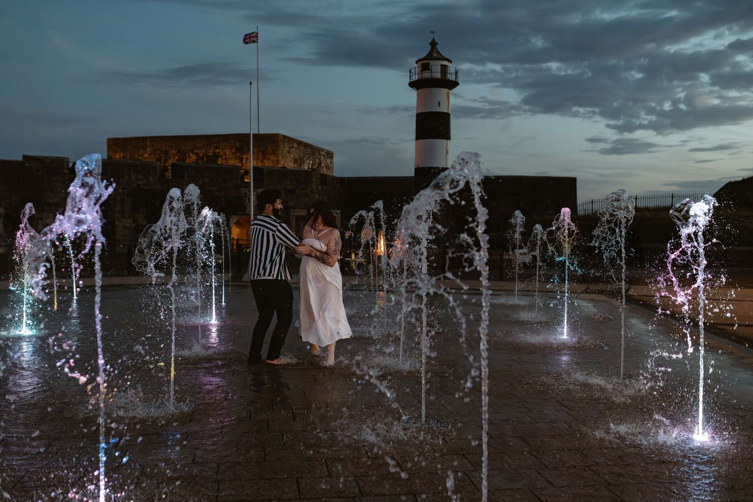Colorful illuminated fountains create a magical nighttime display with figures in silhouette.