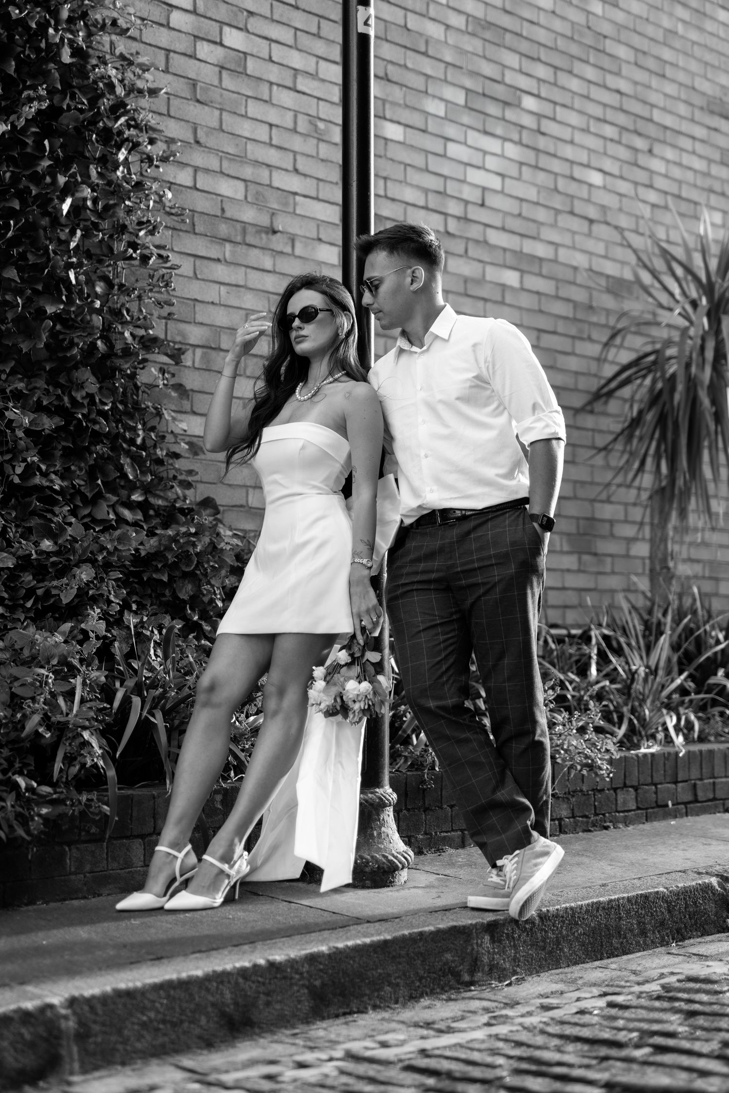 Black and white series of a couple in contrasting outfits sitting on a curb with foliage backdrop.