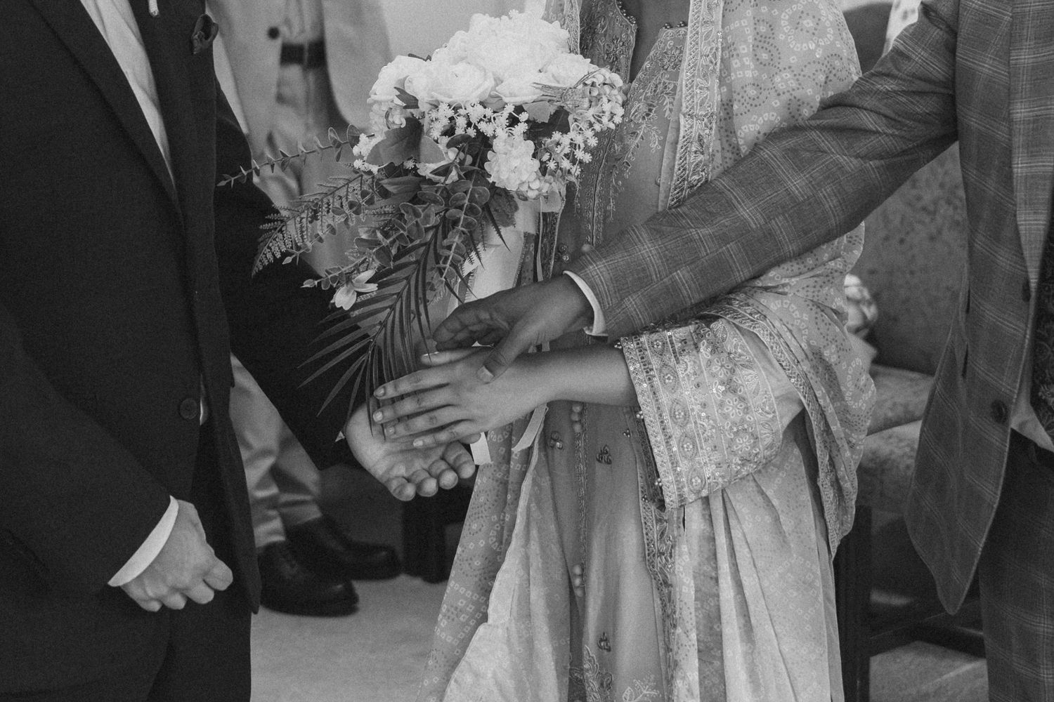 A black and white wedding photo showing hands holding a bouquet of white flowers and delicate lace details.