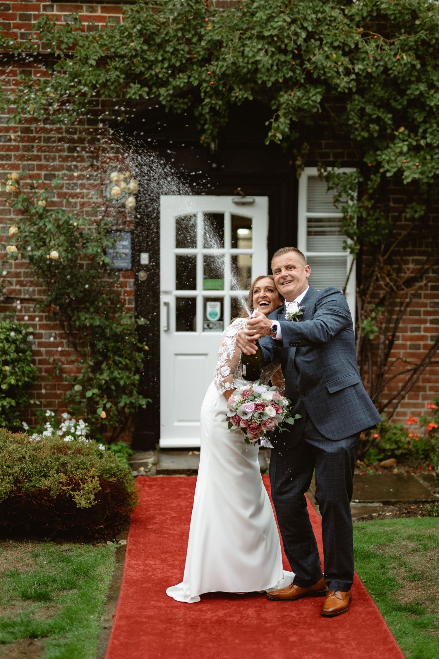 Wedding couple performs playful martial arts poses outdoors on a red carpet.