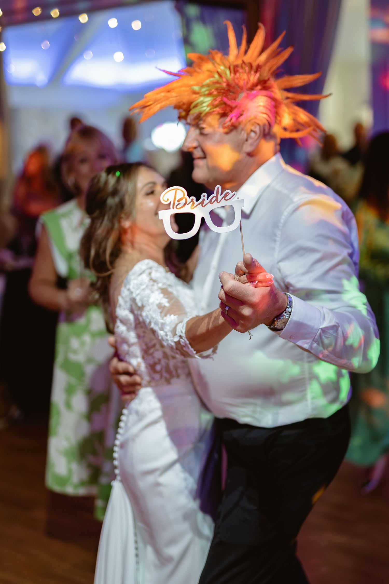 Couples dancing energetically at wedding reception with colorful lighting effects.