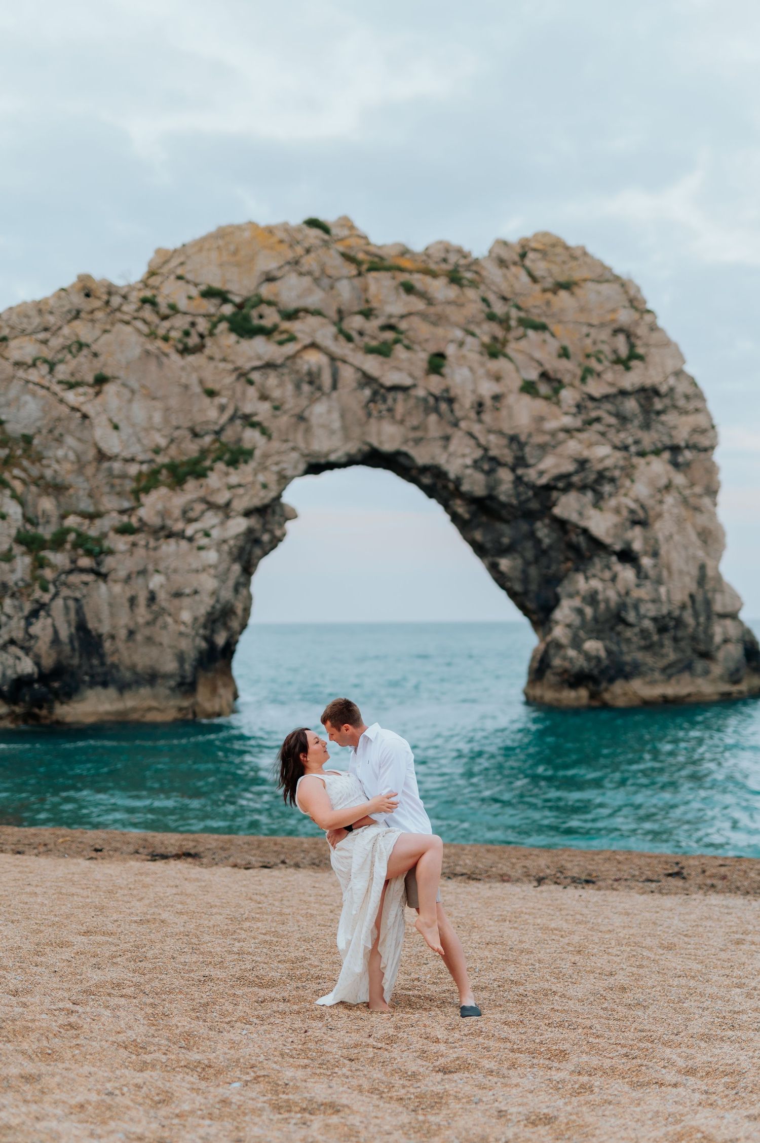 Romantic couple dancing near a natural stone arch formation by the ocean.
