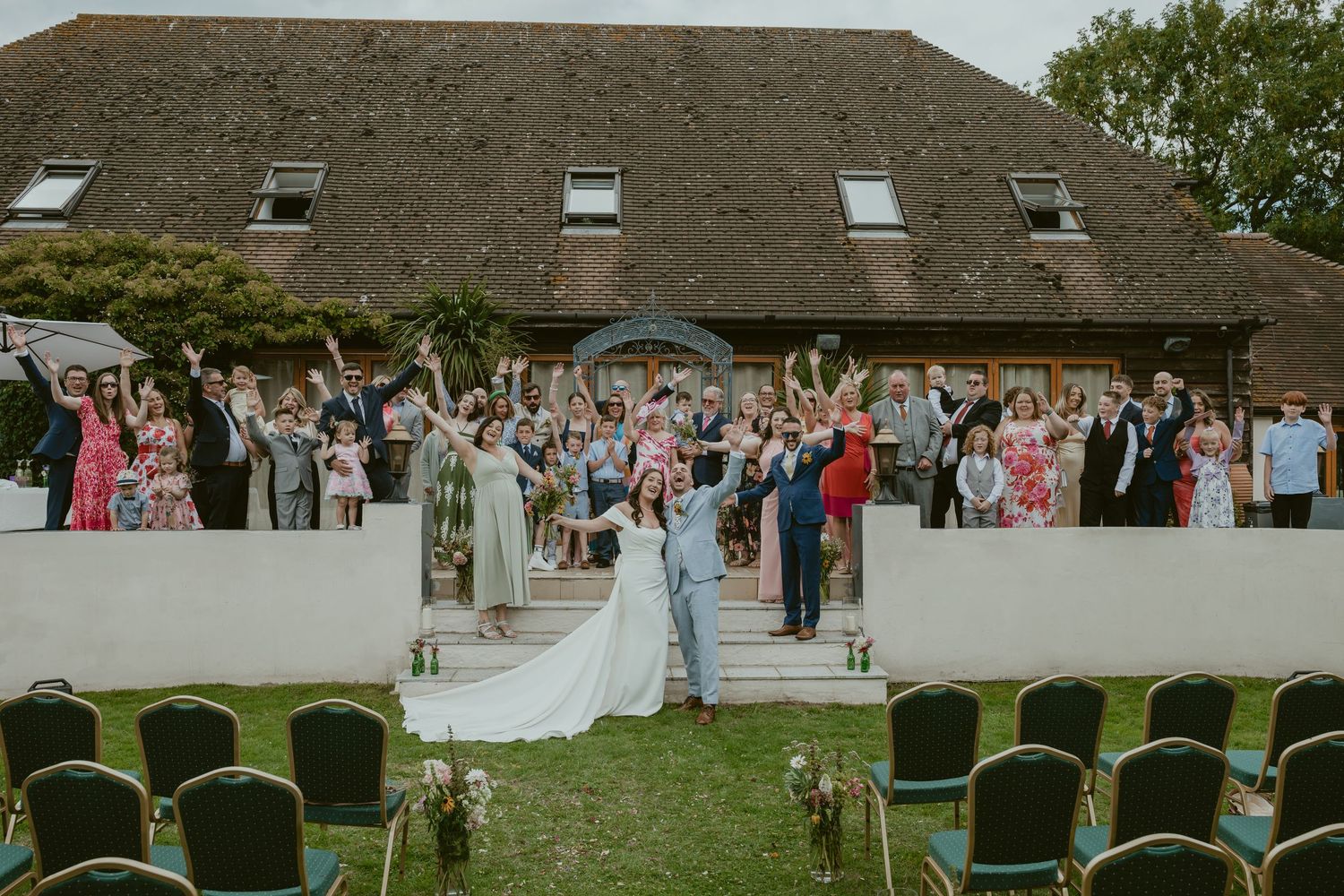 Wedding ceremony setup with green chairs arranged on a lawn in front of a rustic stone building.