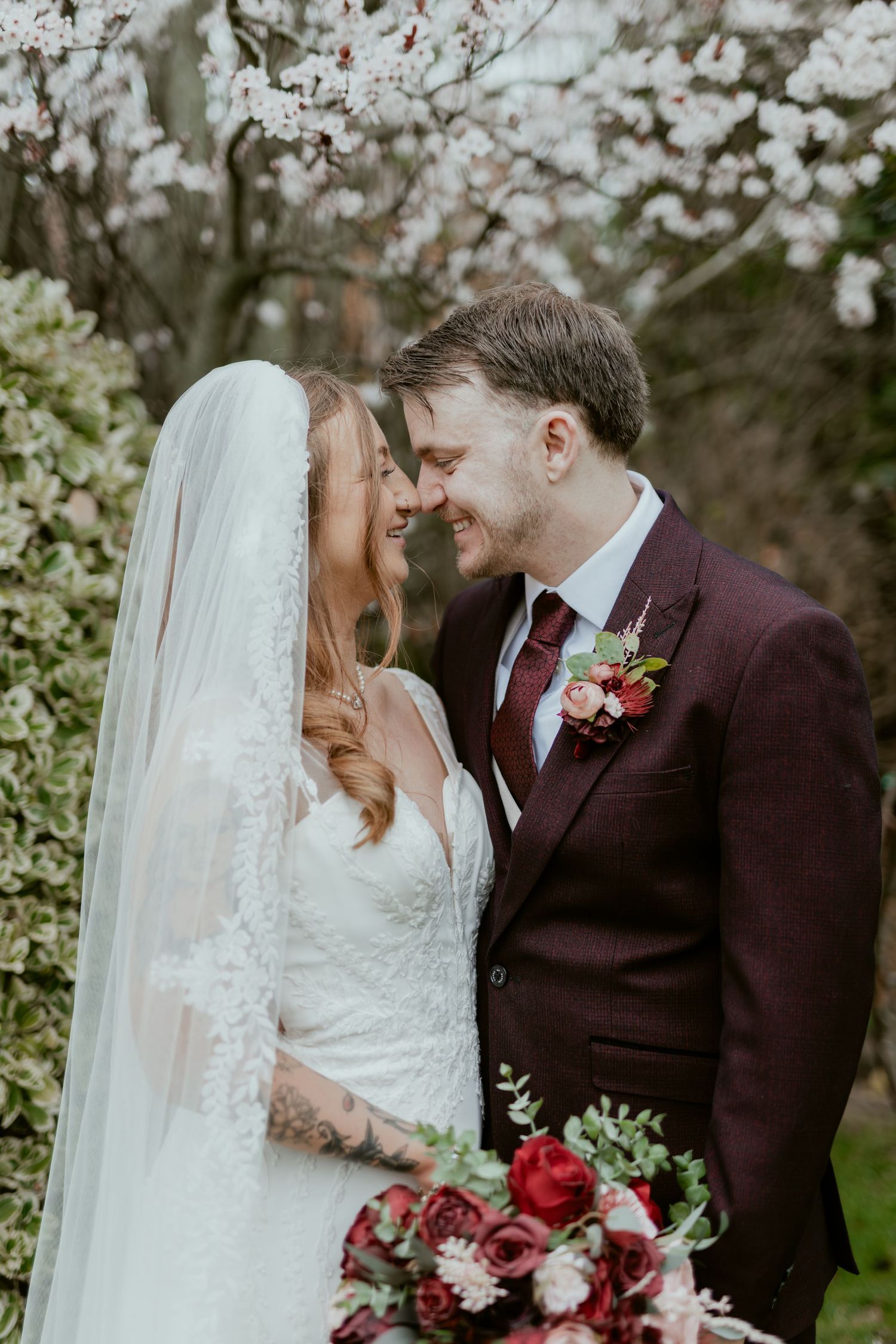 A romantic wedding couple shares intimate moments among blooming spring cherry blossoms in a garden setting.