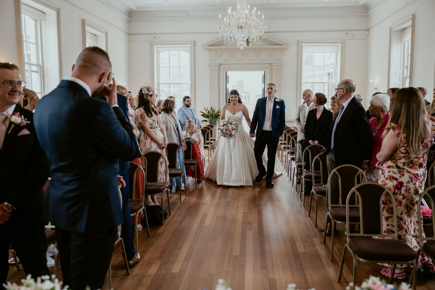 Elegant wedding ceremony in a grand ballroom with crystal chandeliers and hardwood floors.