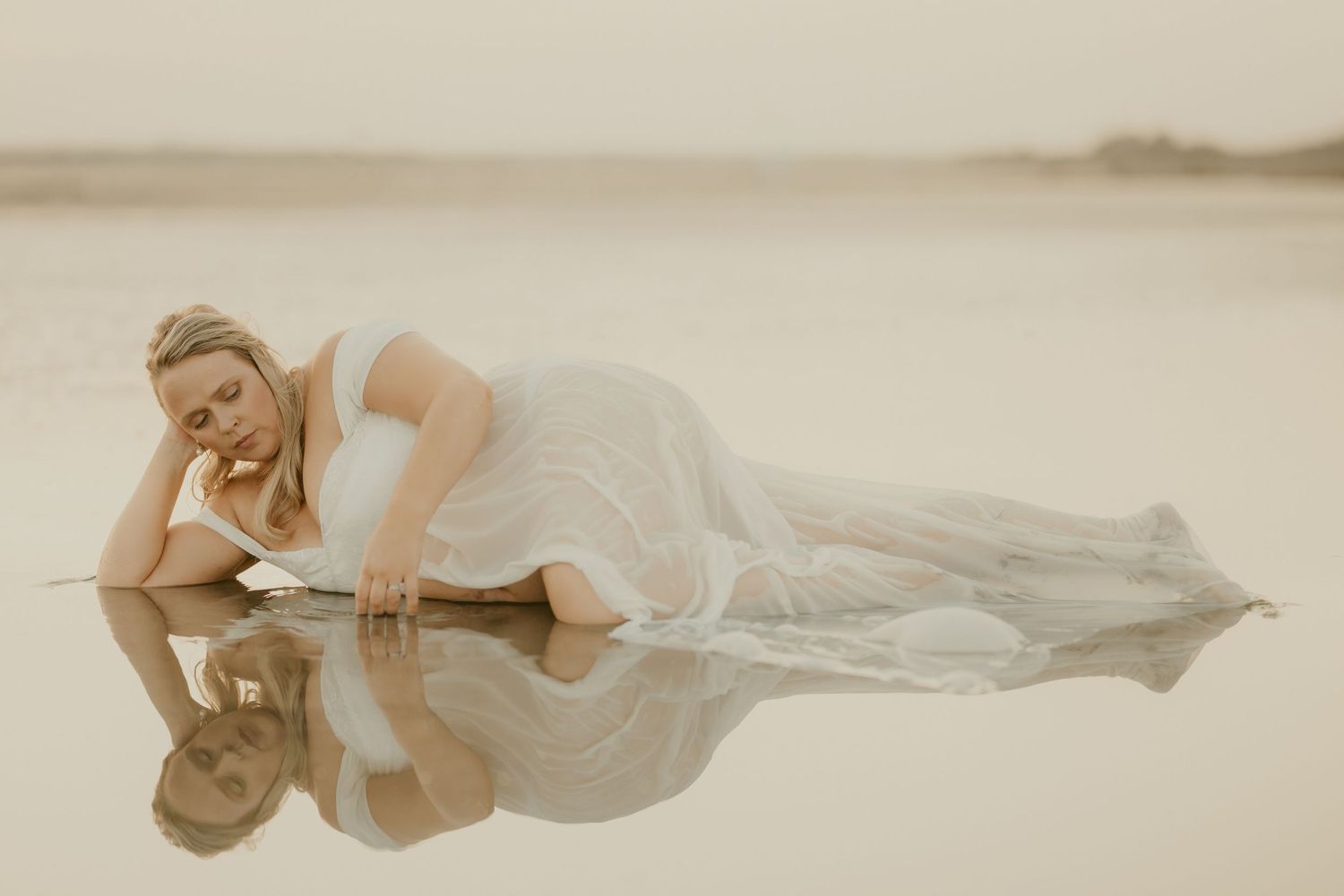 Dreamy beach photoshoot featuring flowing white dress in shallow water.