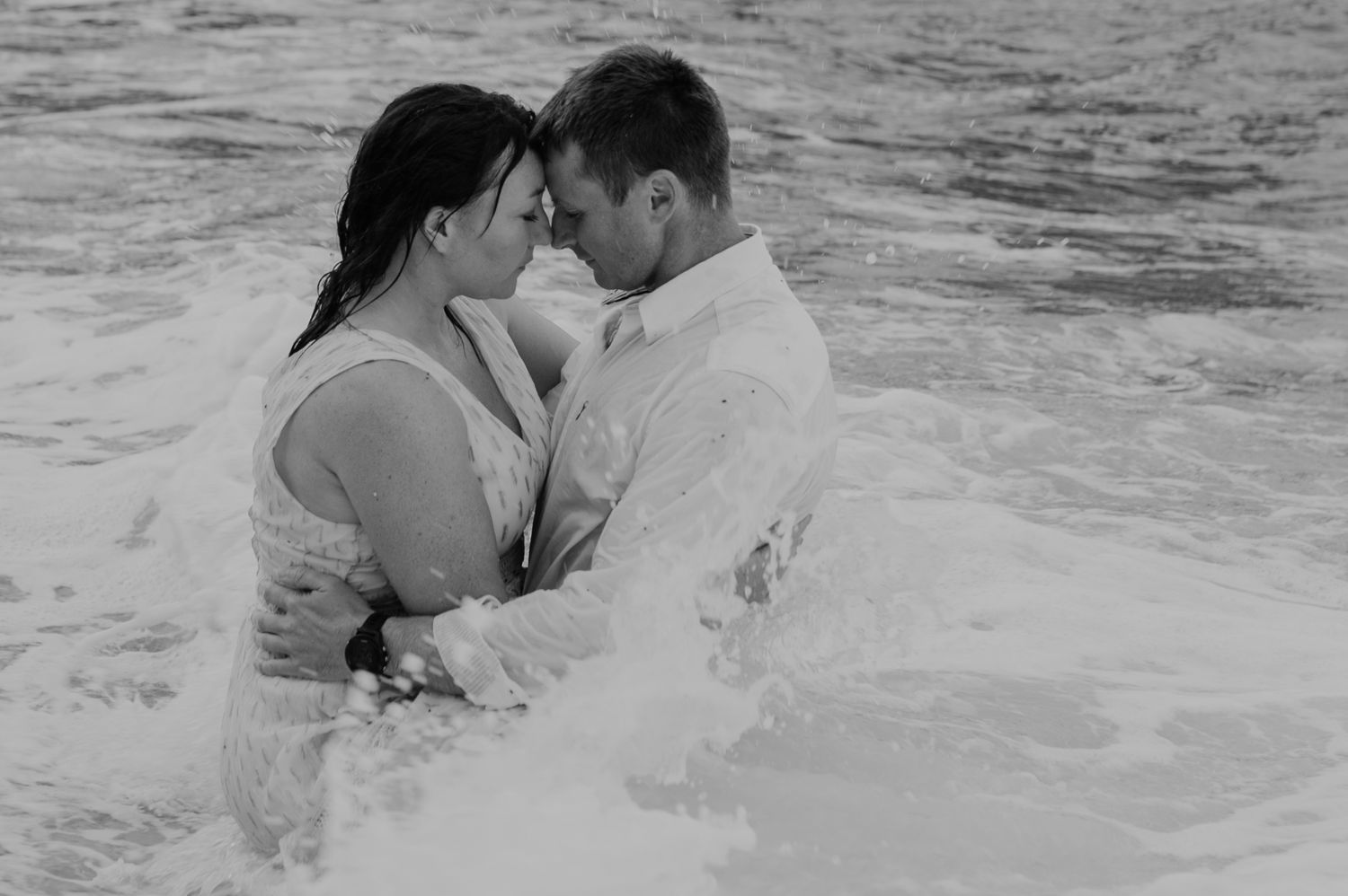 A couple shares romantic moments in the ocean waves at the beach.