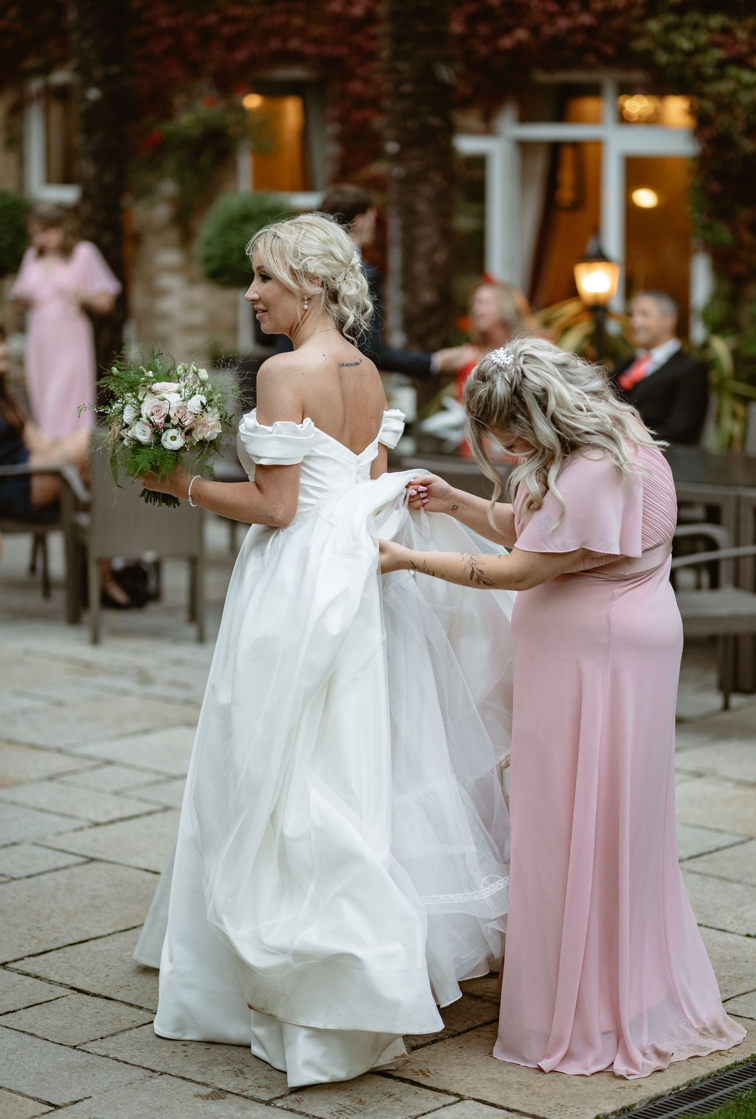 Bride in white gown dancing with bridesmaids in pink dresses on stone patio.