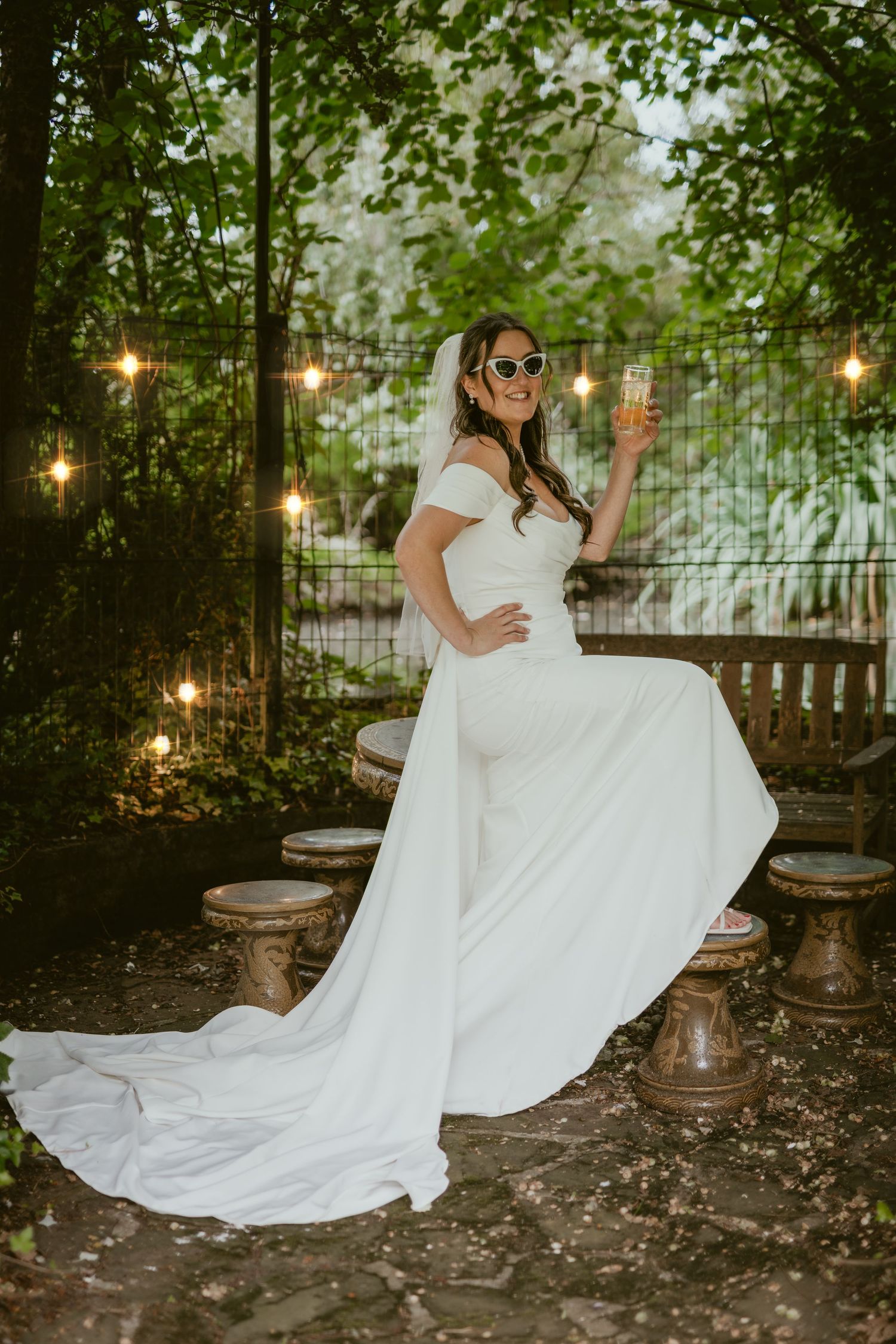 Bride twirls in a flowing white dress under garden string lights at dusk.