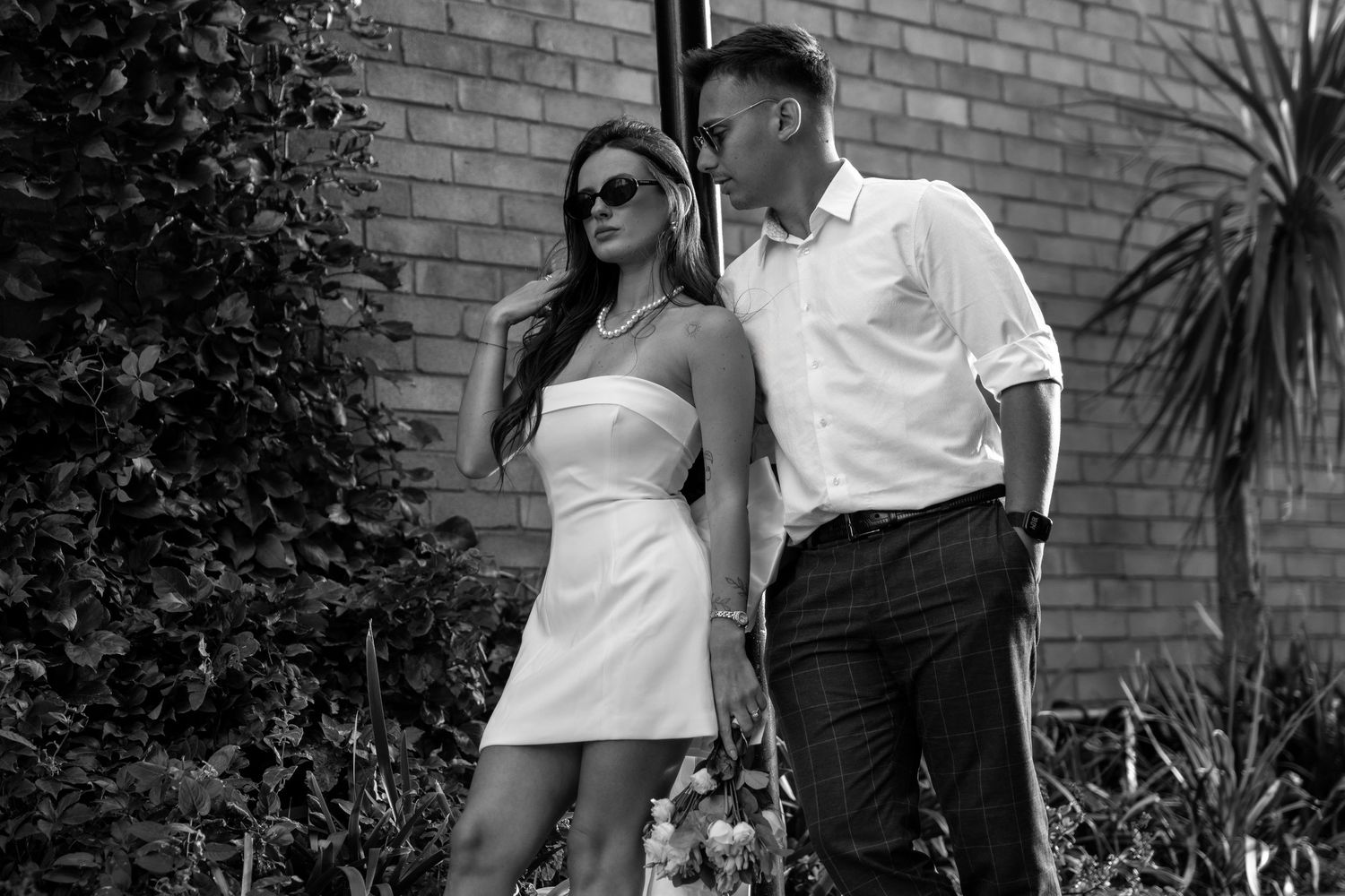 Romantic couple poses in front of a rustic brick wall during an engagement photoshoot.