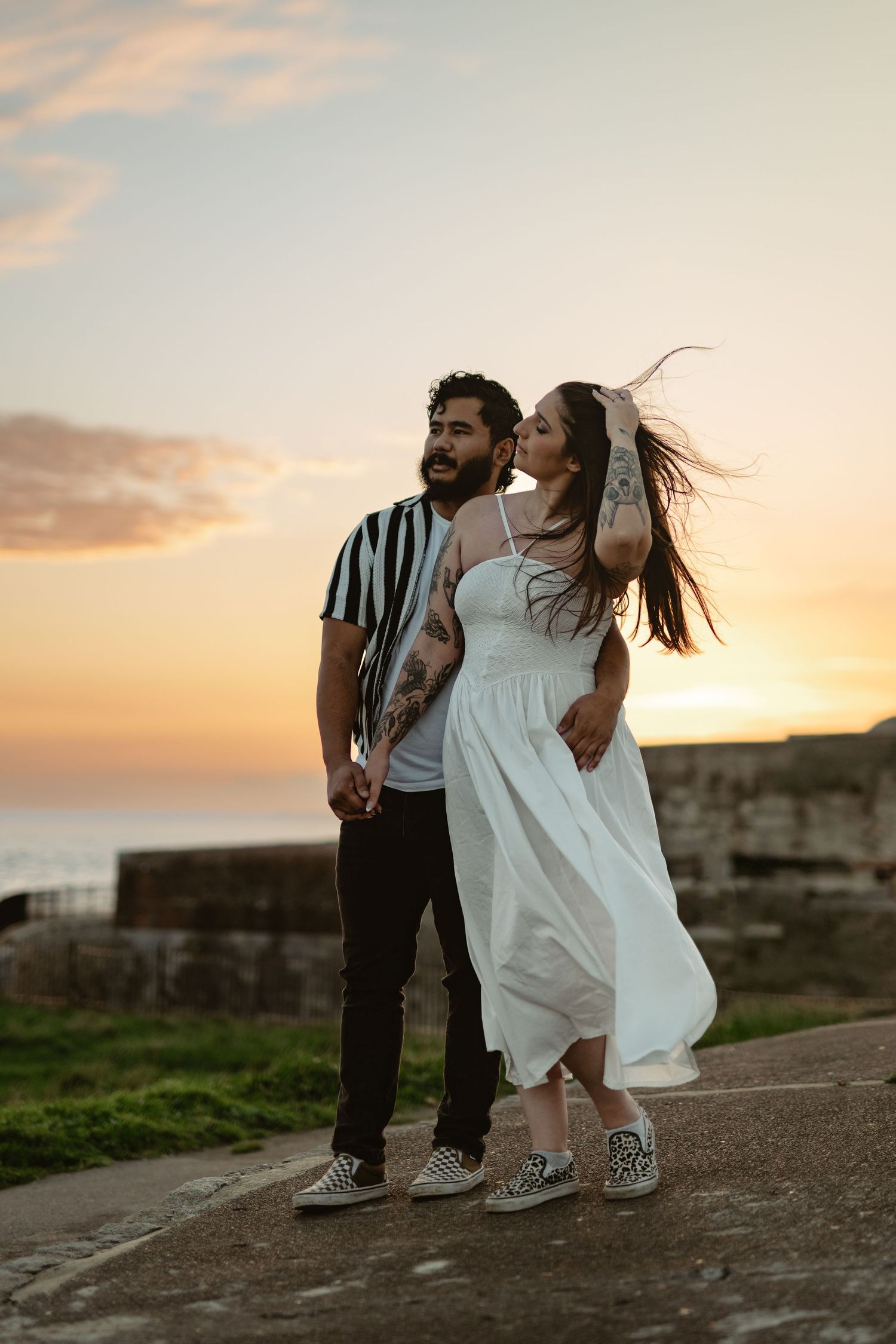 A couple in contrasting outfits dances together at sunset by the ocean.