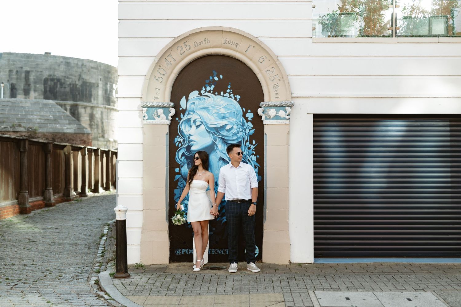 People walking past white building facade with arched doorways.