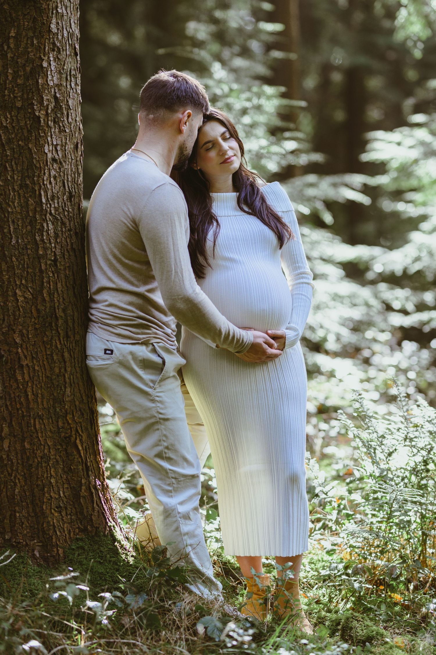A couple embraces in a wooded setting during a maternity photography session.