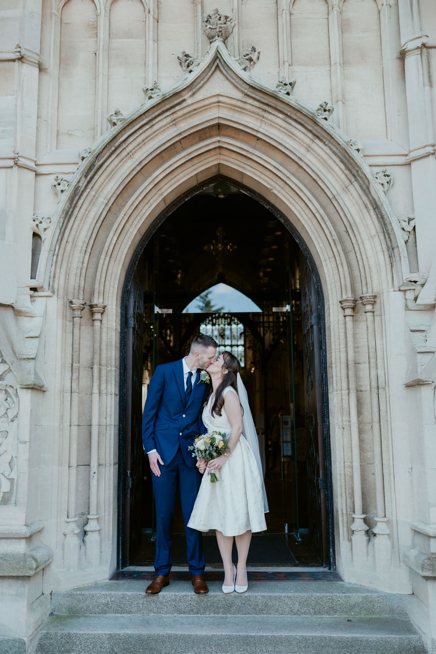 A couple poses in a gothic stone archway entrance during a wedding ceremony.