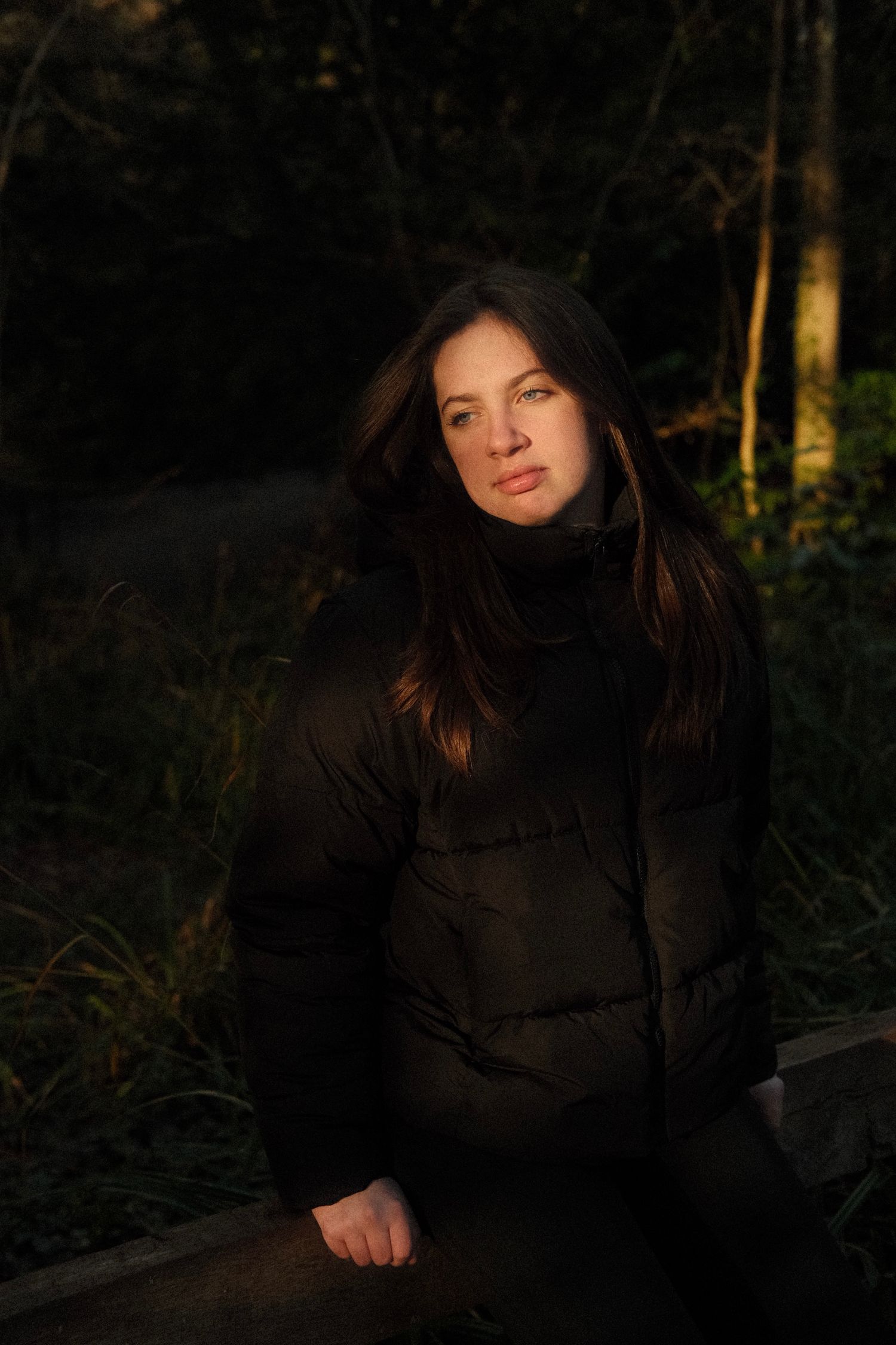 A dark and moody portrait taken in a forest setting with dramatic shadows.