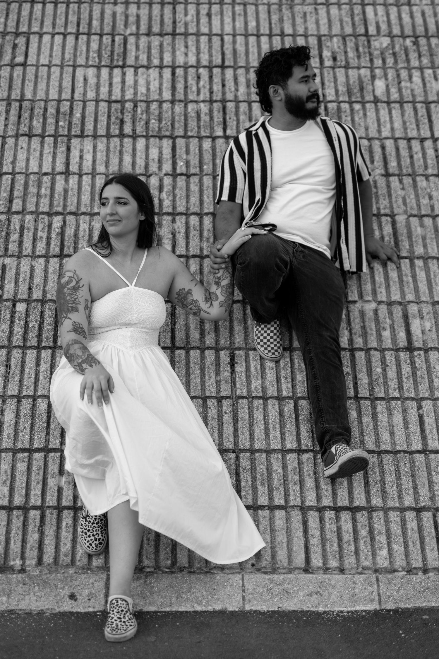 A couple in contrasting black and white outfits pose against a brick wall in an artistic composition.