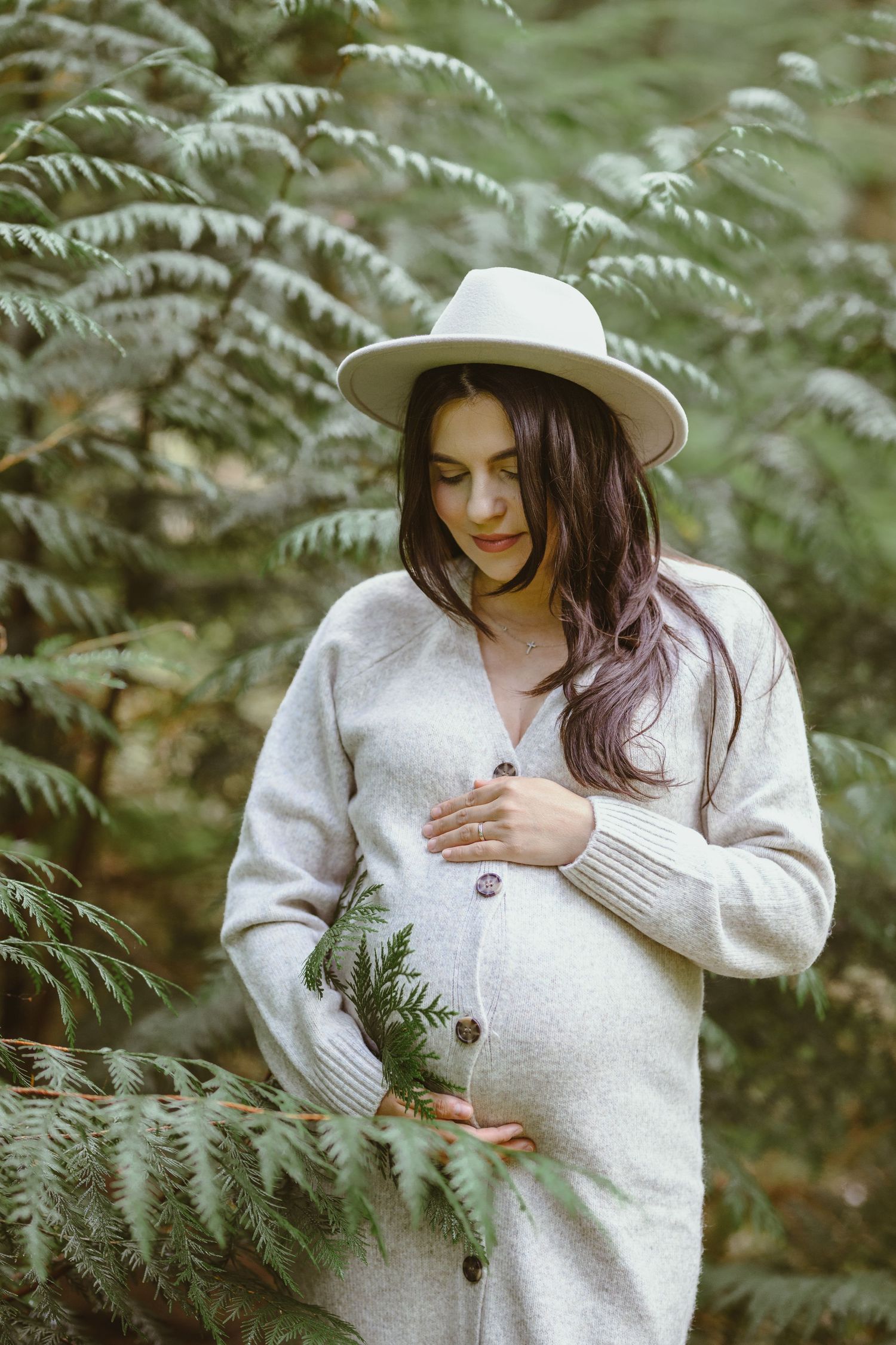 Maternity portrait in cozy sweater among ferns in forest setting.