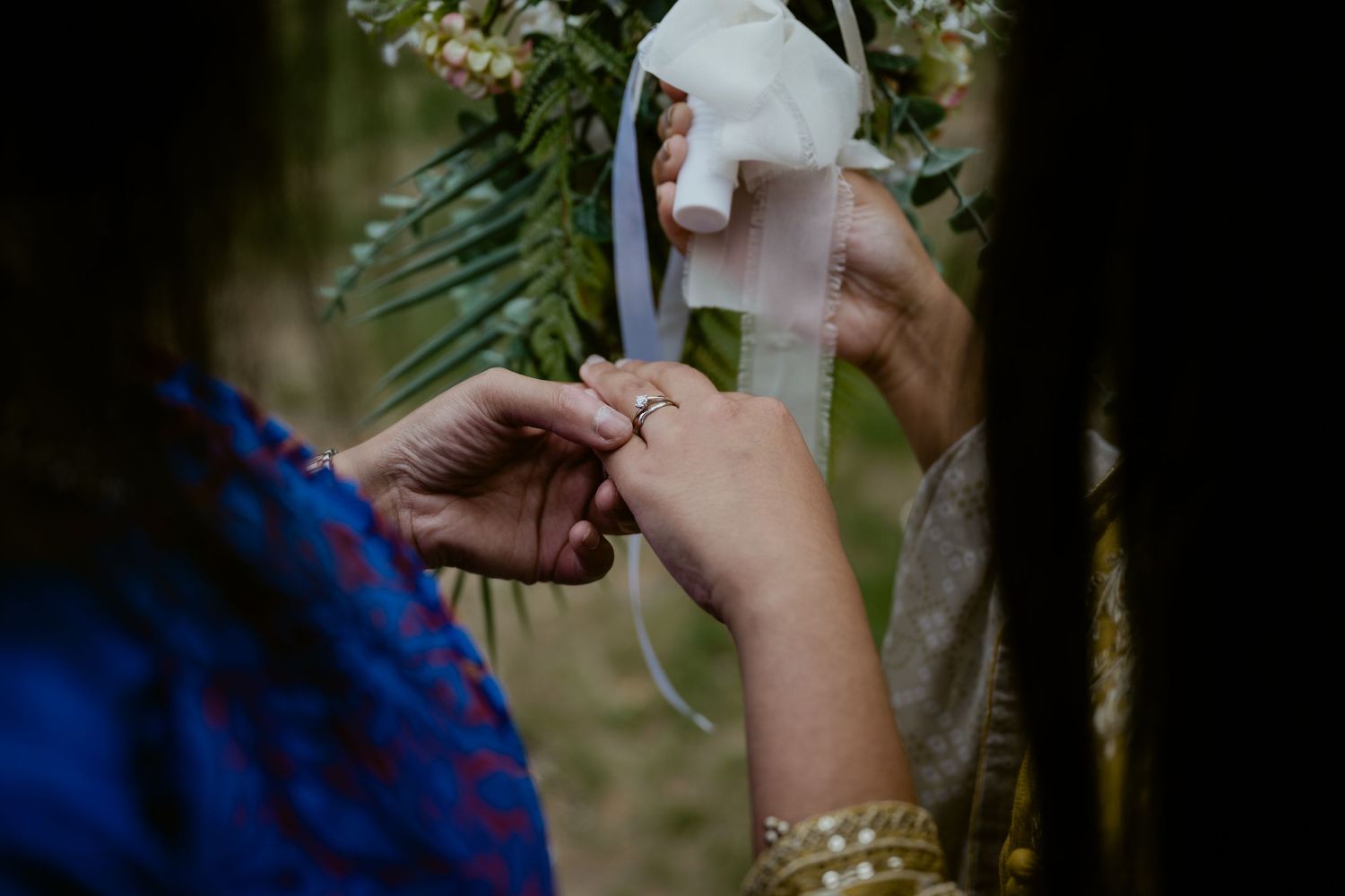 Close-up shot of hands exchanging rings during an outdoor ceremony.