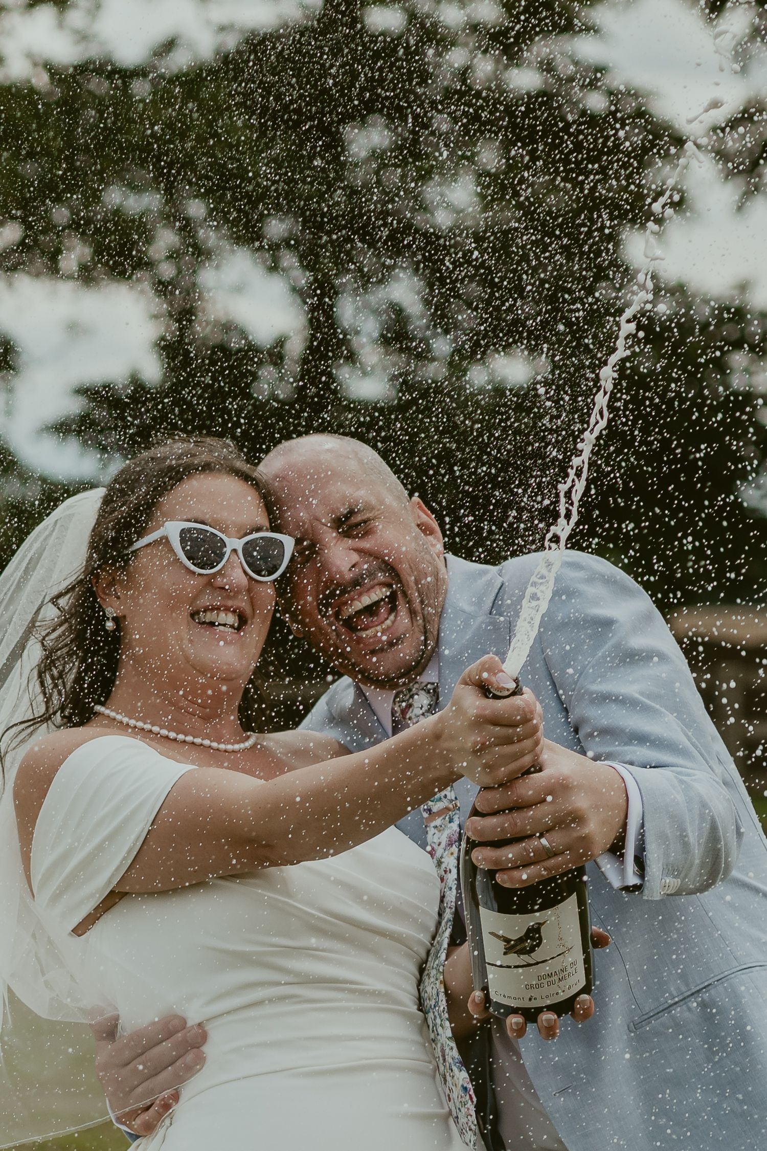 Celebratory moment with champagne spray during outdoor wedding photos.